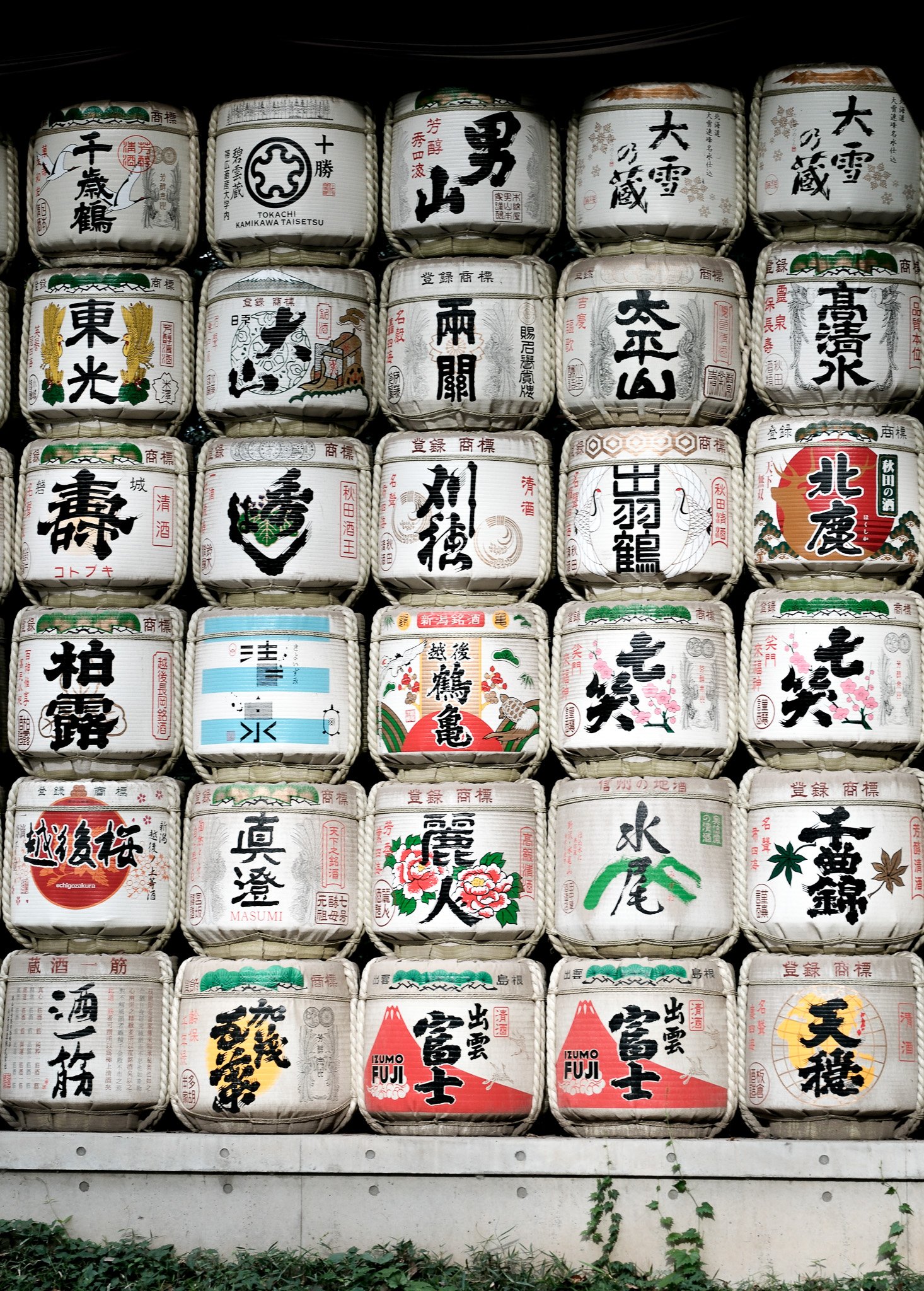 Mehrere traditionelle japanische Sake-Fässer, die zu Dekorationszwecken gestapelt sind, mit japanischen Schriftzeichen und traditionellen Designs.