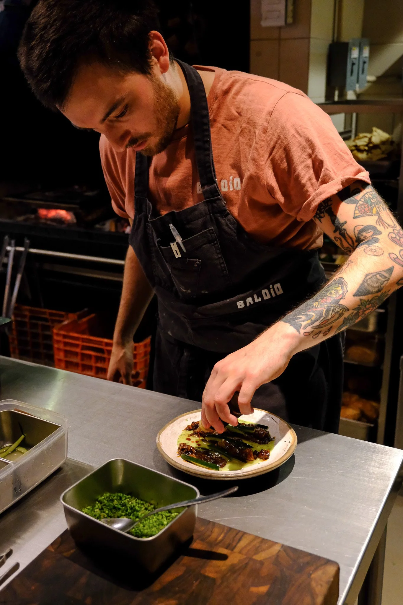 Ein tätowierter Koch dekantiert Grillfleisch auf einem Teller in einer professionellen Küche.