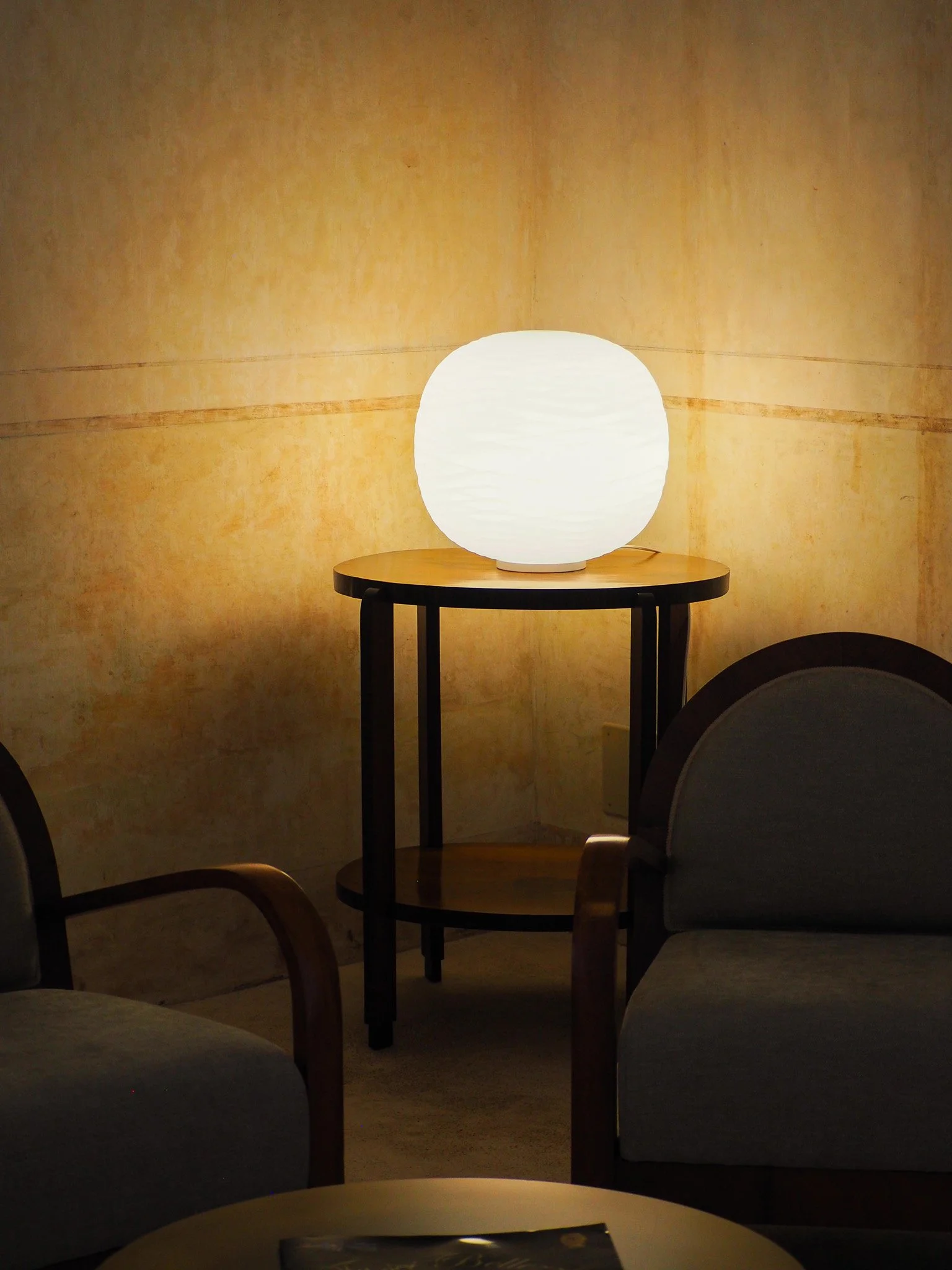 Ein runder, weißen Lampenschirm auf einem kleinen Holztisch in einem Raum mit beige Wand.