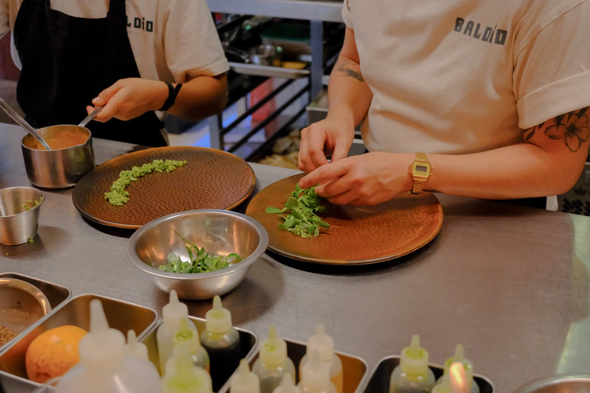 Personen bereiten auf einem Tisch vor, grünes Gemüse zu schneiden. Es gibt verschiedene Küchenutensilien und Flaschen mit Saucen oder Dressings auf dem Tisch.