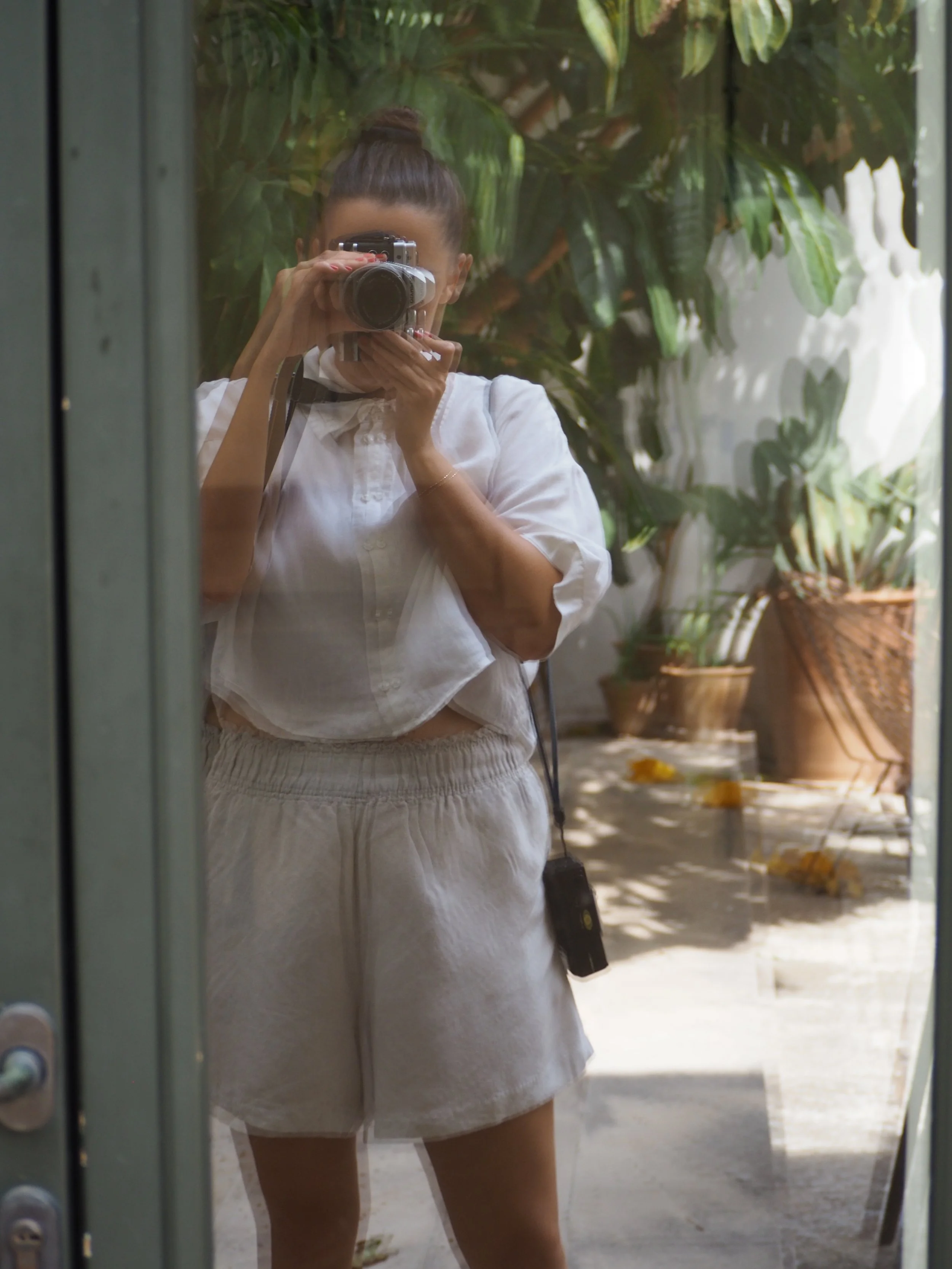 Frau nimmt Selbstporträt mit Spiegelreflexkamera vor einem begrünten Hintergrund.