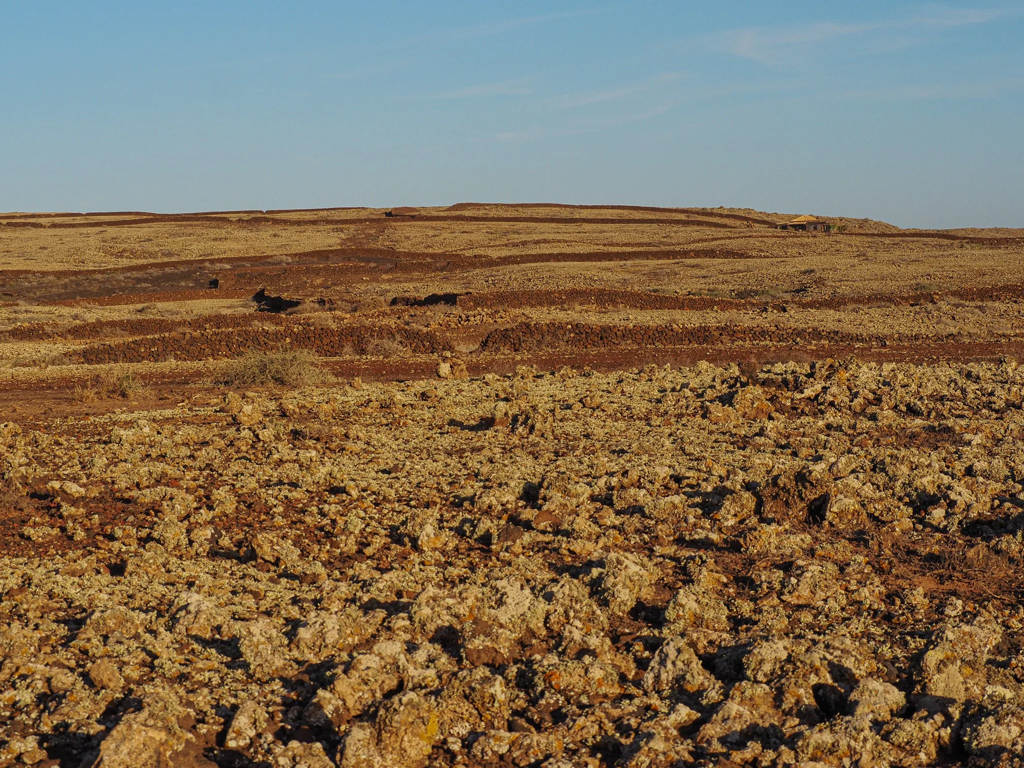 Terrassenartige Felsen- und Kieslandschaft unter blauem Himmel in einer Wüstenumgebung.
