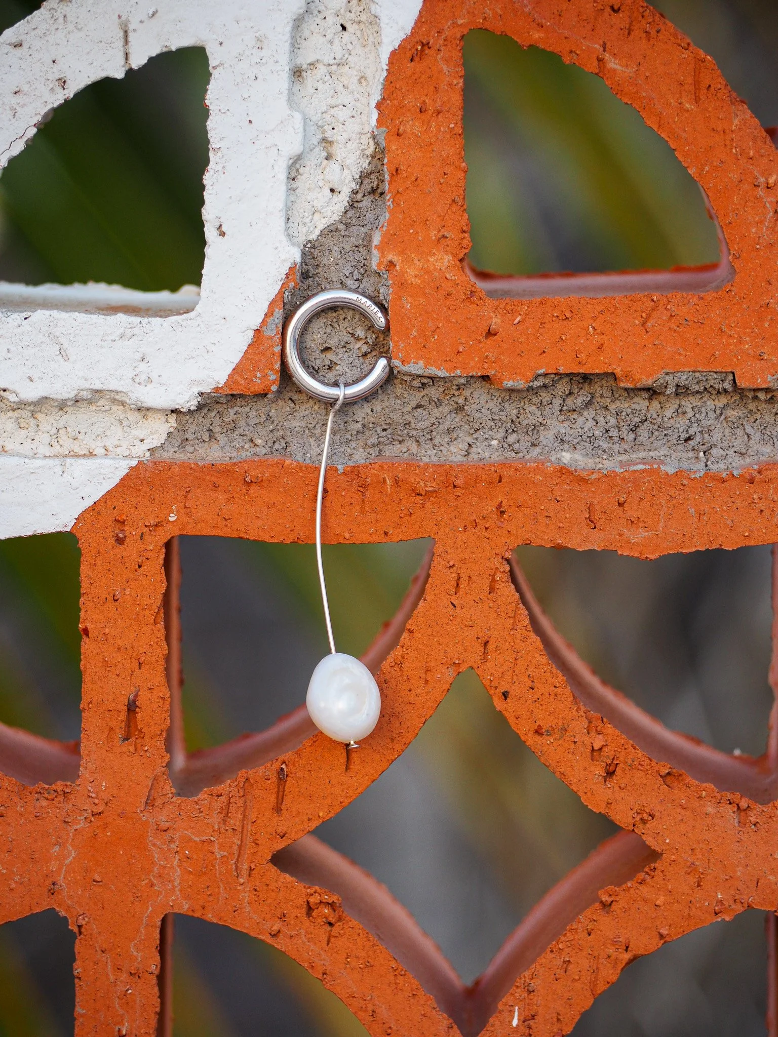 Ein Blick auf eine Ziegelmauer aus roten und weißen Ziegeln mit einem silbernen Ringe, an dem eine Perle hängt.