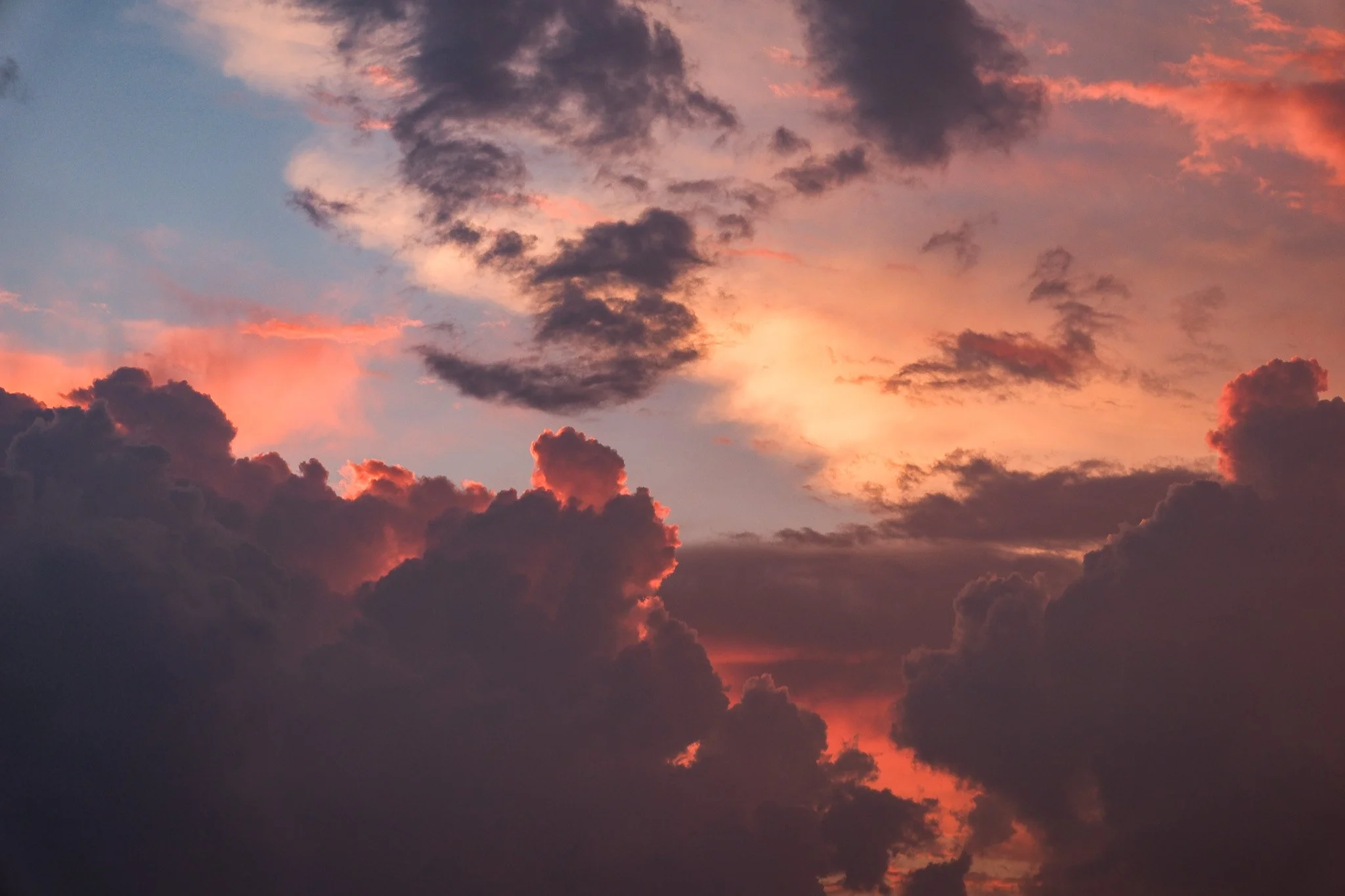 Ein Himmel mit dunklen Wolken bei Sonnenuntergang, die Scene zeigt Wolken in verschiedenen Farben wie Grau, Rosa und Orange.