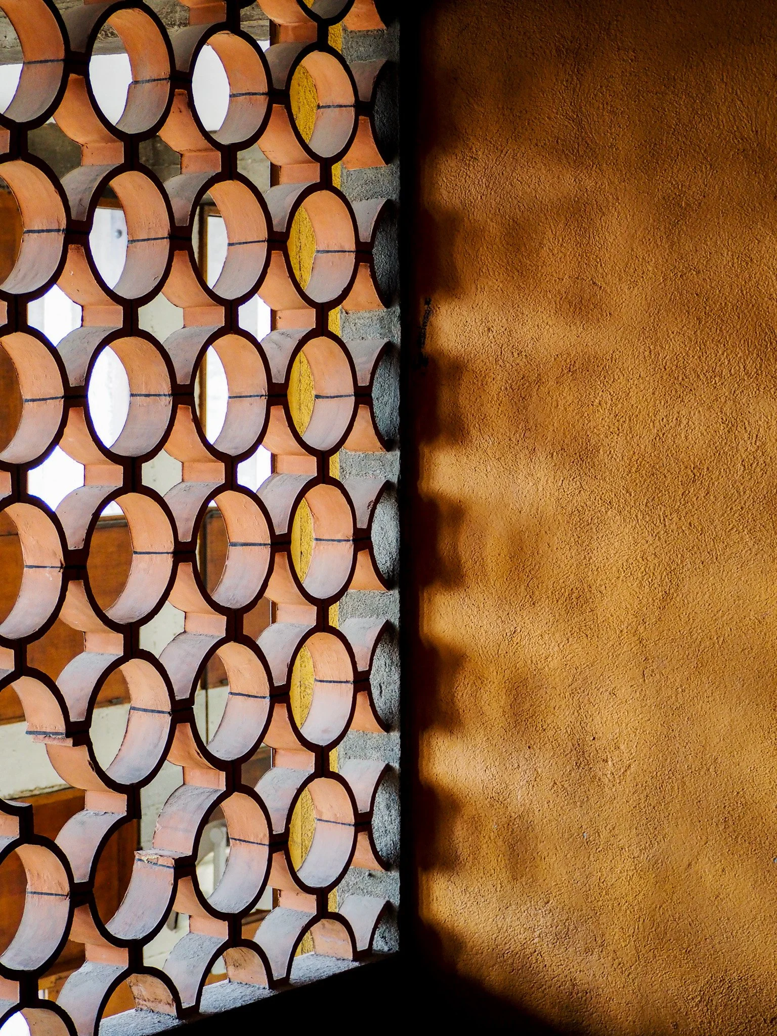 Blick durch ein Gitter aus runden Tonpfannen auf eine Wand aus Ziegeln und Holzrahmen.