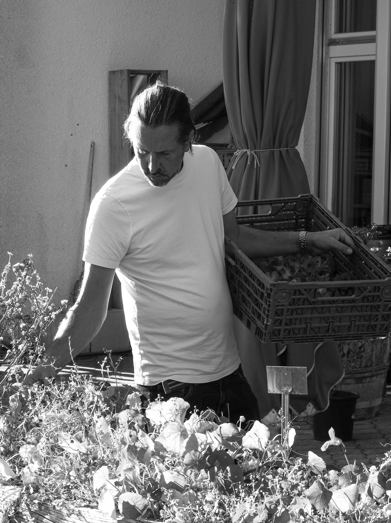 Ein Mann beim Pflanzen auf einem Balkon, mit einer Tüte voll Pflanzen und einem Gemüsegarten.
