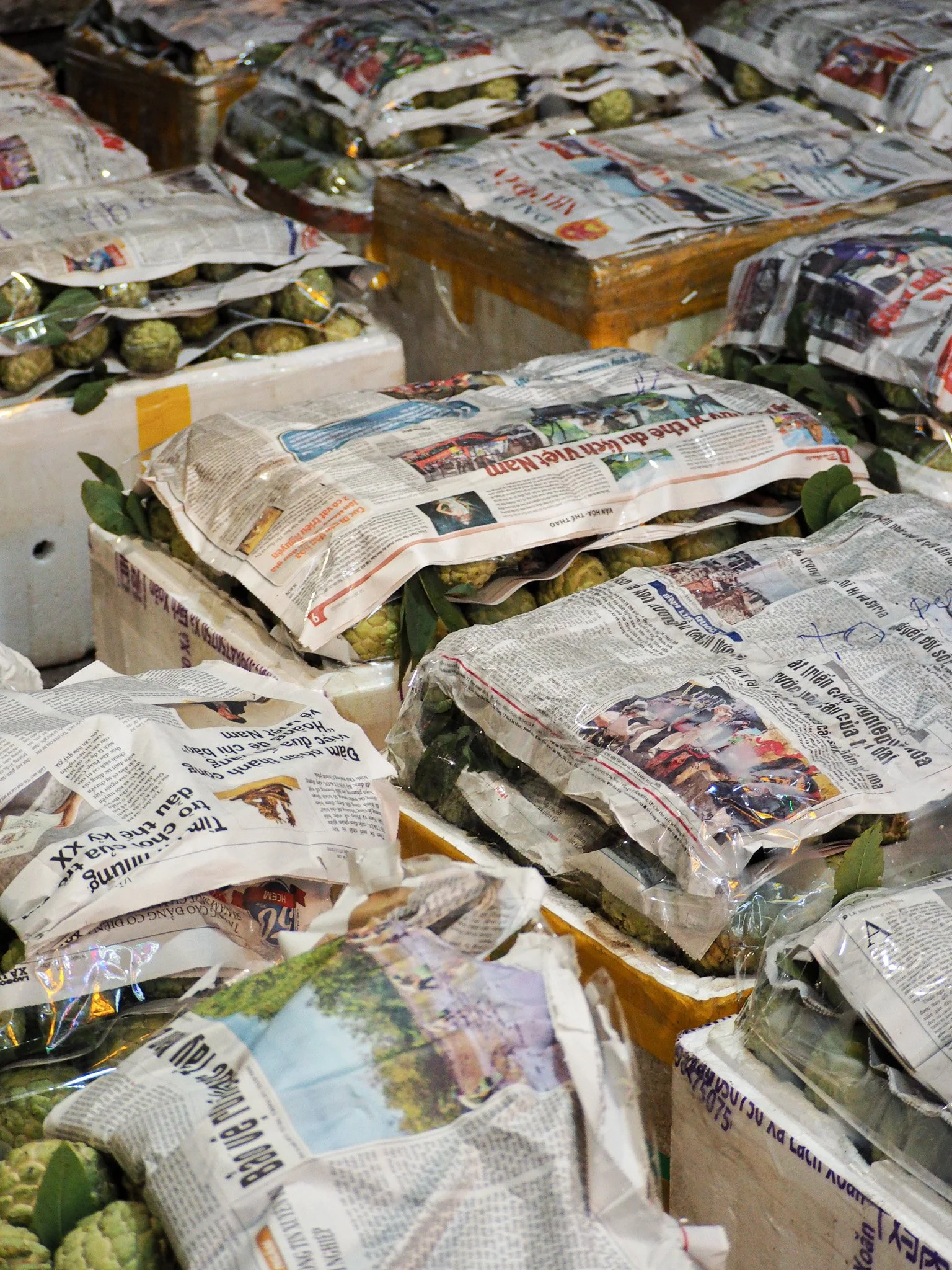 Mehrere Pakete mit grünen Früchten, eingewickelt in Zeitungspapier, auf einer Lagertheke