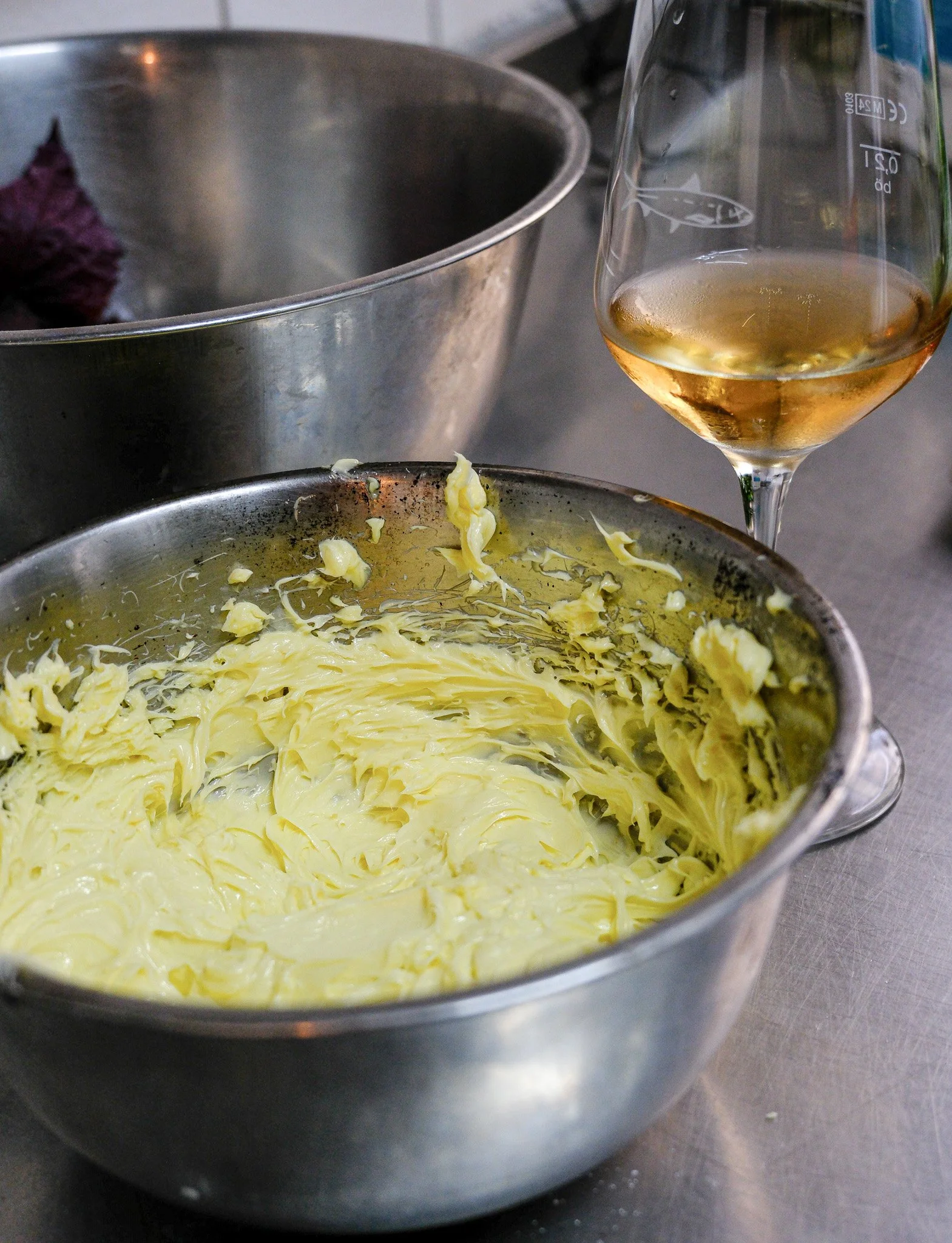 Ein Metallbehälter mit geschmolzener Butter, ein Weinglas mit weißem Wein und ein weiterer metallener Behälter im Hintergrund.