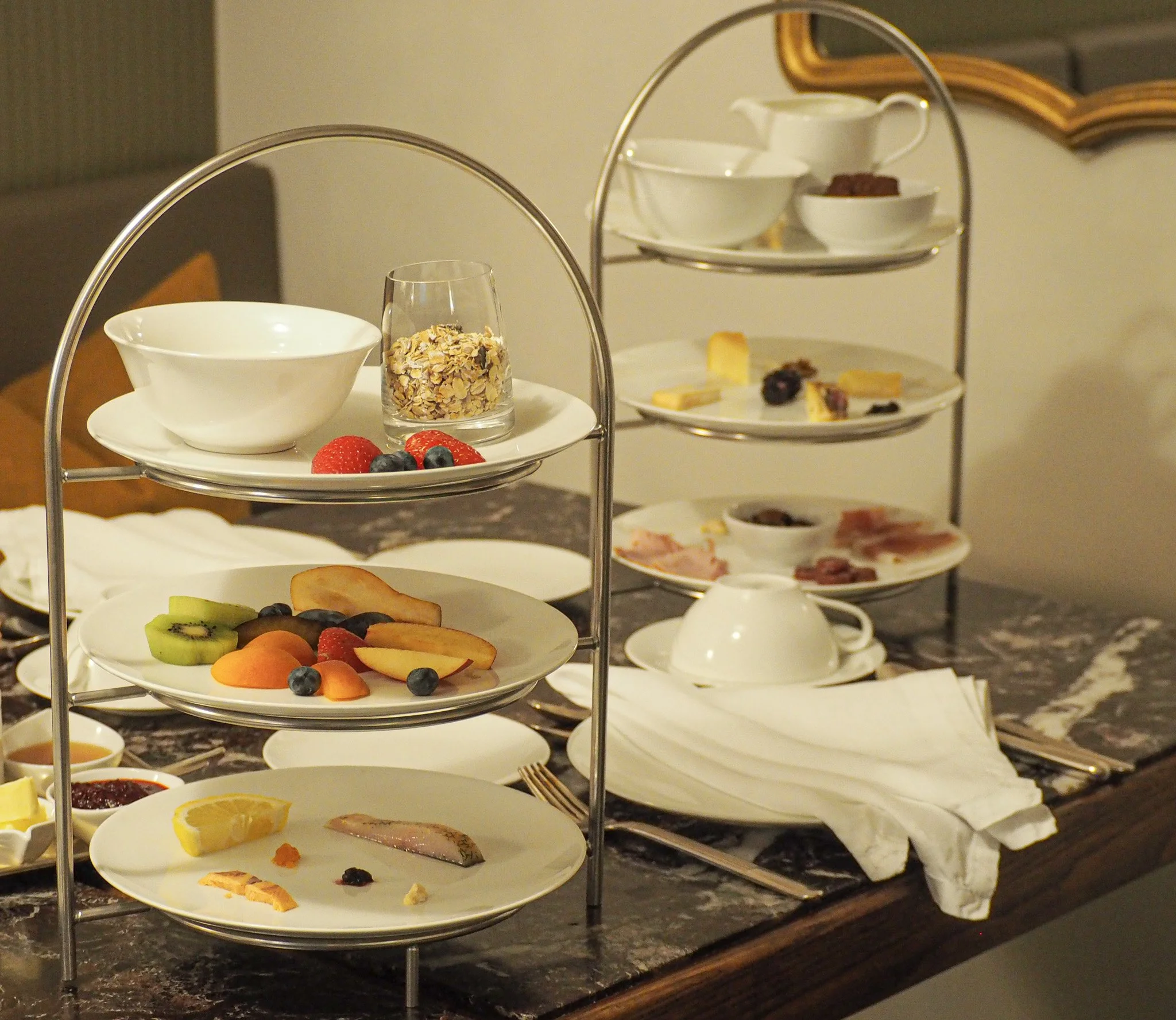 Frühstücksteller mit Obst, Marmelade, Käse, Schinken, Joghurt, Müsli und Tee auf einem Frühstückstisch.