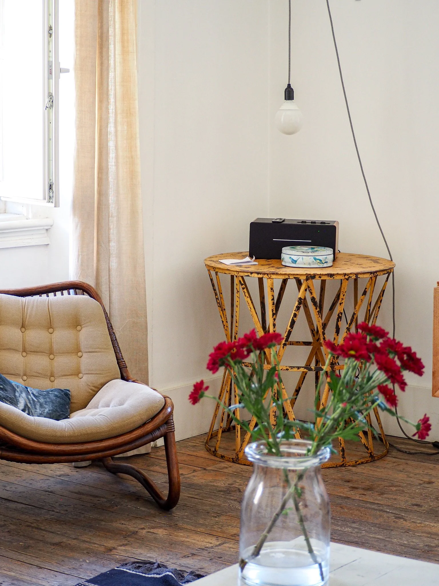 Ein Wohnzimmer mit einem Fenster, einer beige Couch, einem runden Holzsideboard, einer Vase mit roten Blumen und einem Holzfußboden.