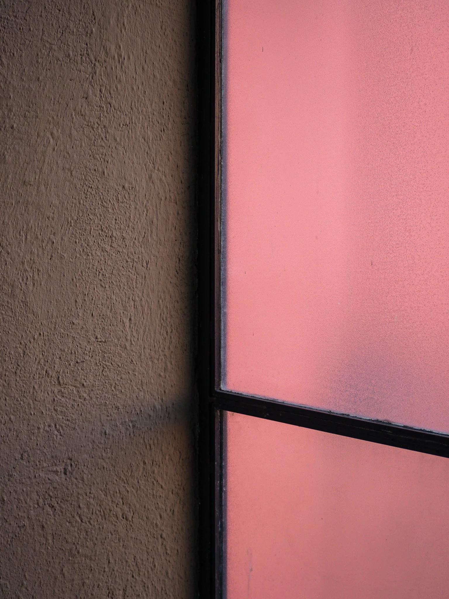 Blick auf eine Fensterfront mit Milchglas, das bei Sonnenuntergang rosa leuchtet, und eine braune Wand im Vordergrund.