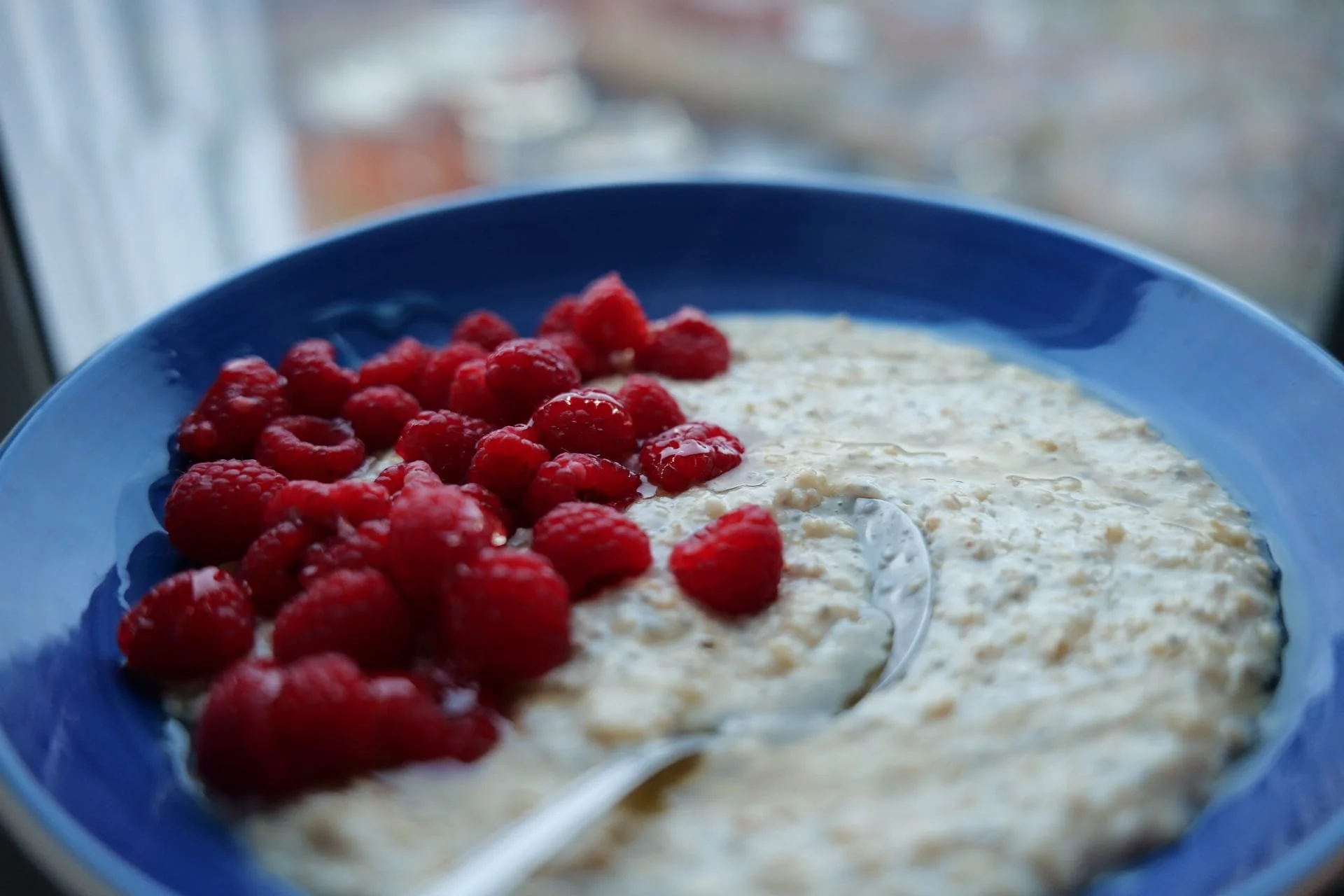 A blue bowl contains oatmeal topped with fresh red raspberries.