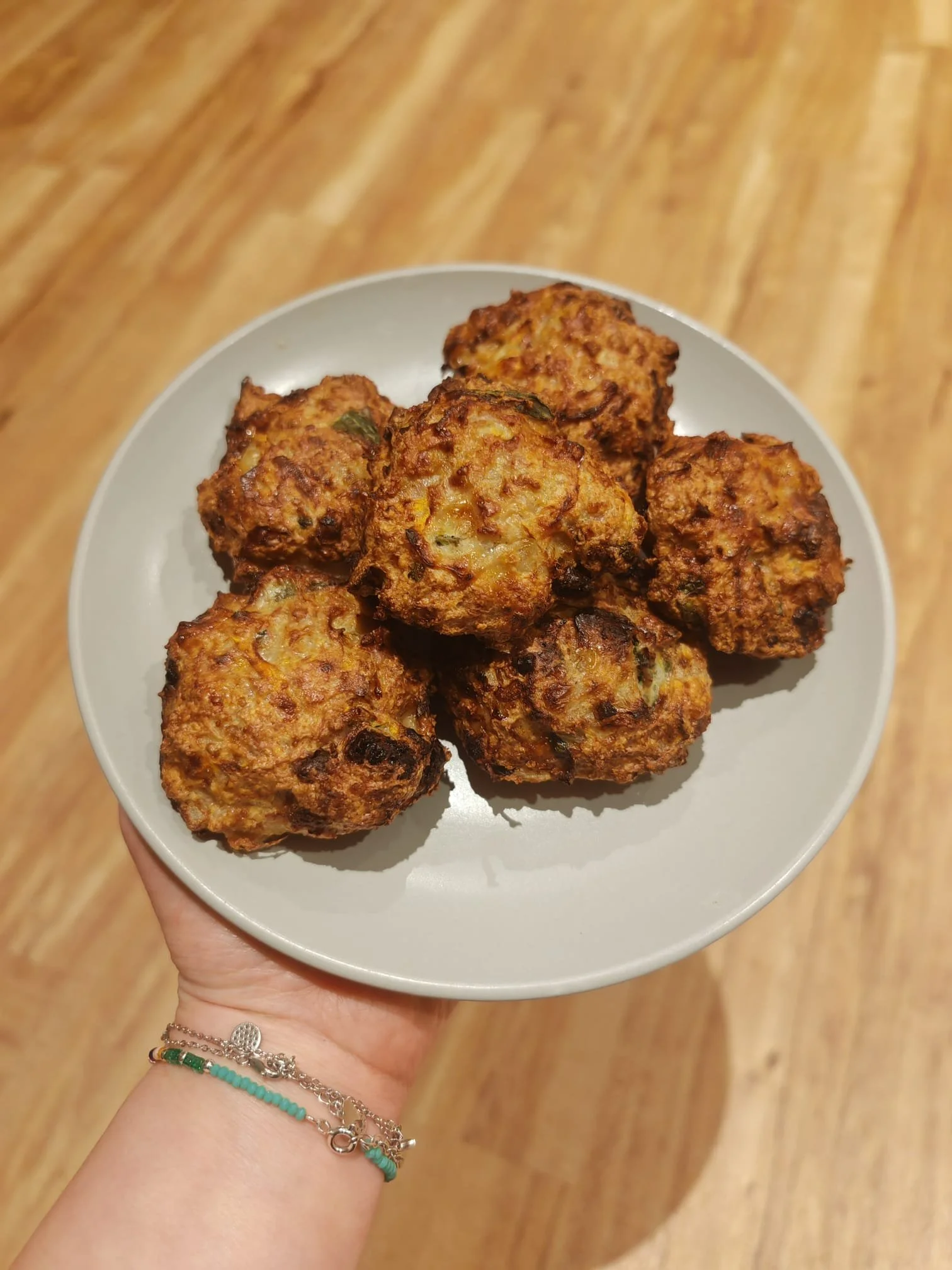 Hand holding a white plate with six fried meatballs, with a wooden background.