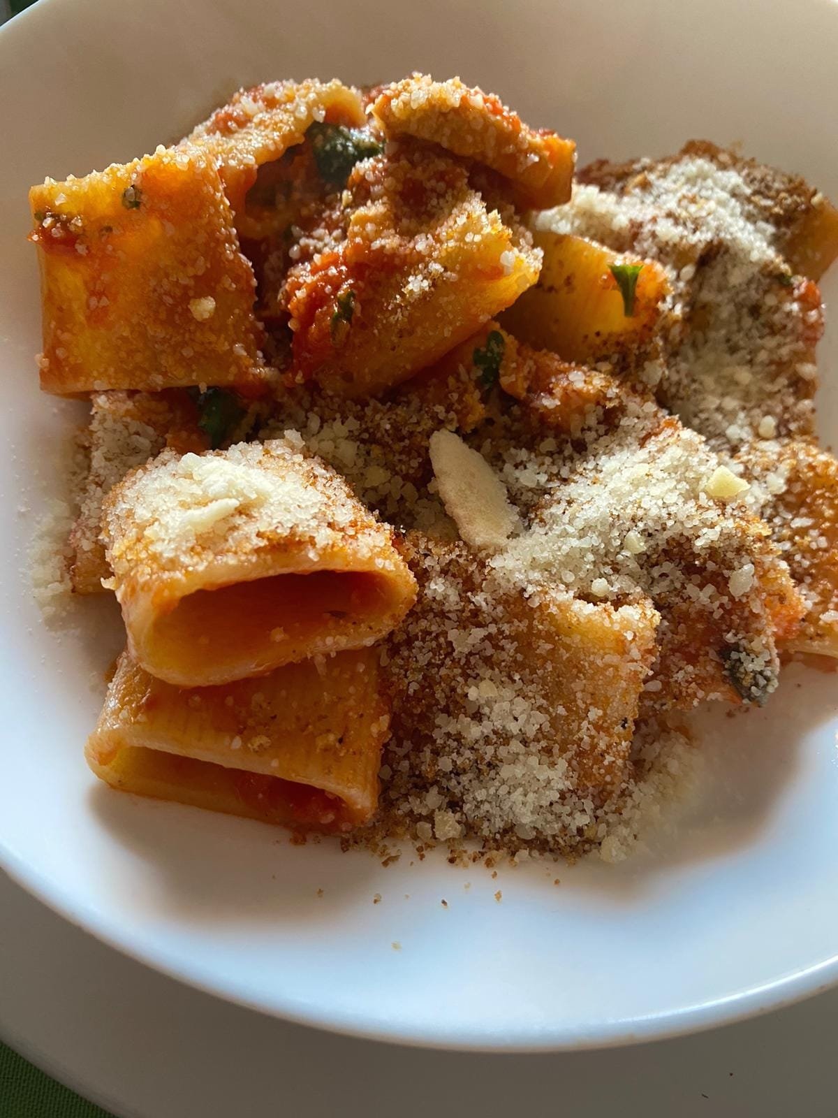 Close-up of a white bowl filled with cooked rigatoni pasta topped with grated cheese and spices.