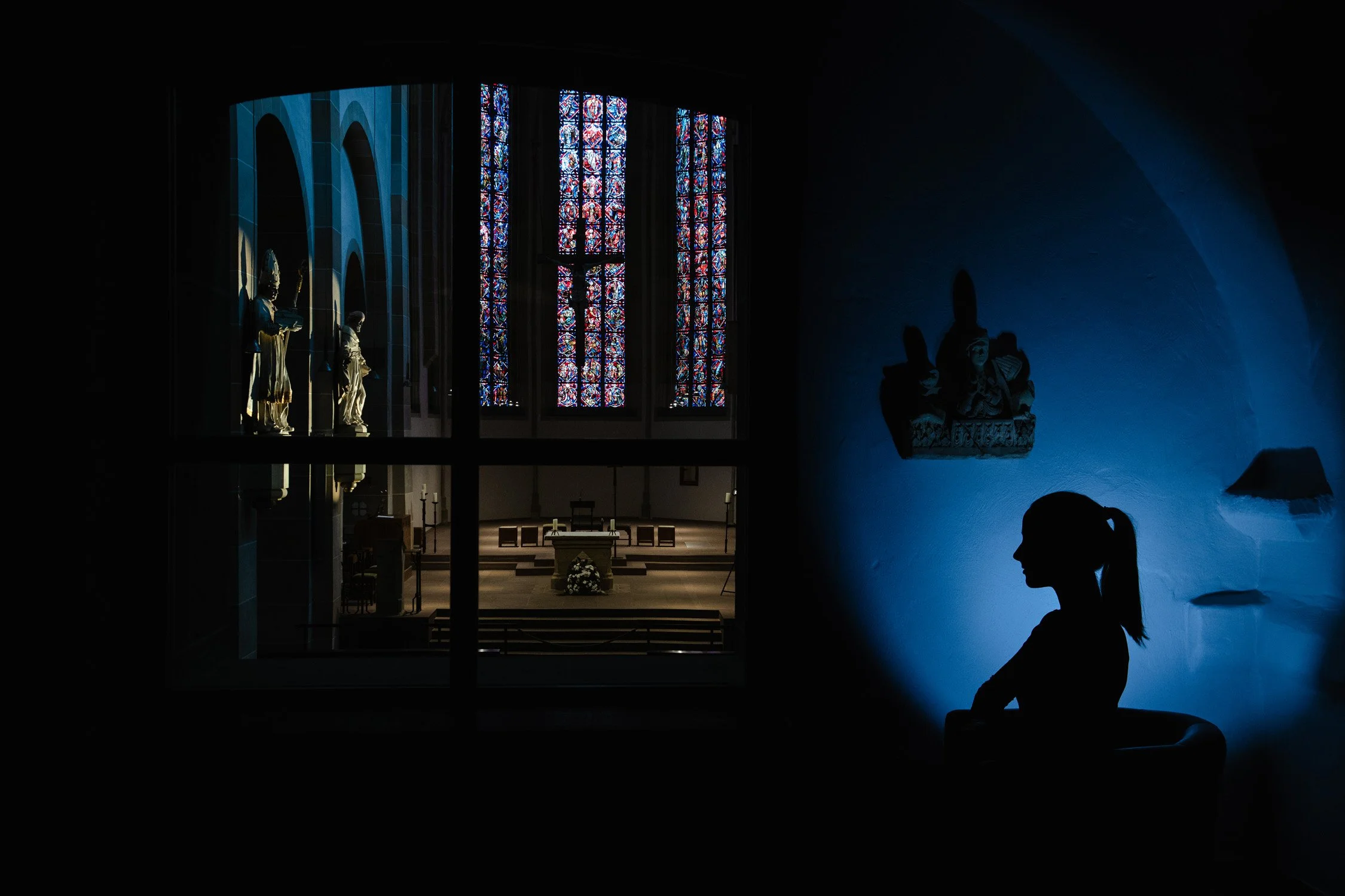 Dunkler Raum mit farbig leuchtenden Fenstern und Silhouette – Architekturfotografie mit atmosphärischer Lichtstimmung