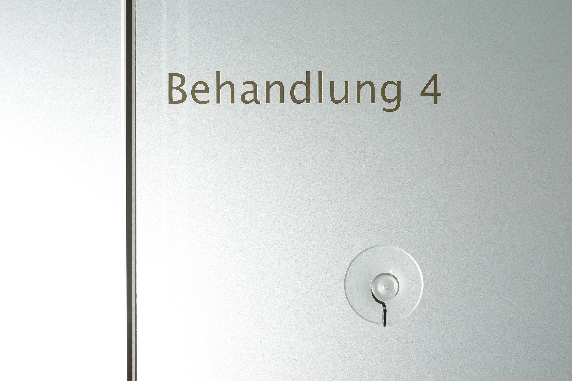Milchglastür mit der Beschriftung „Behandlung 4“ – Unternehmensreportage einer Praxis in Brühl.