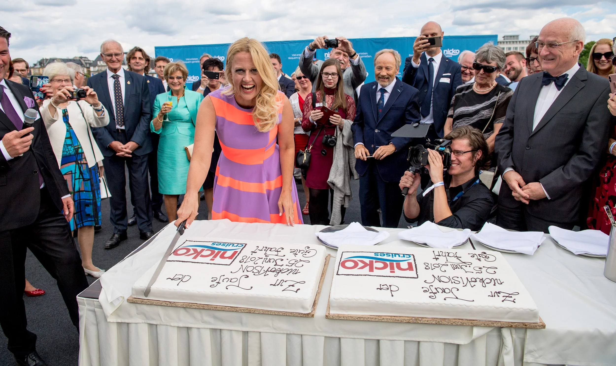 Frau schneidet eine große Torte an, Gäste fotografieren – Eventfotografie einer Schiffstaufe