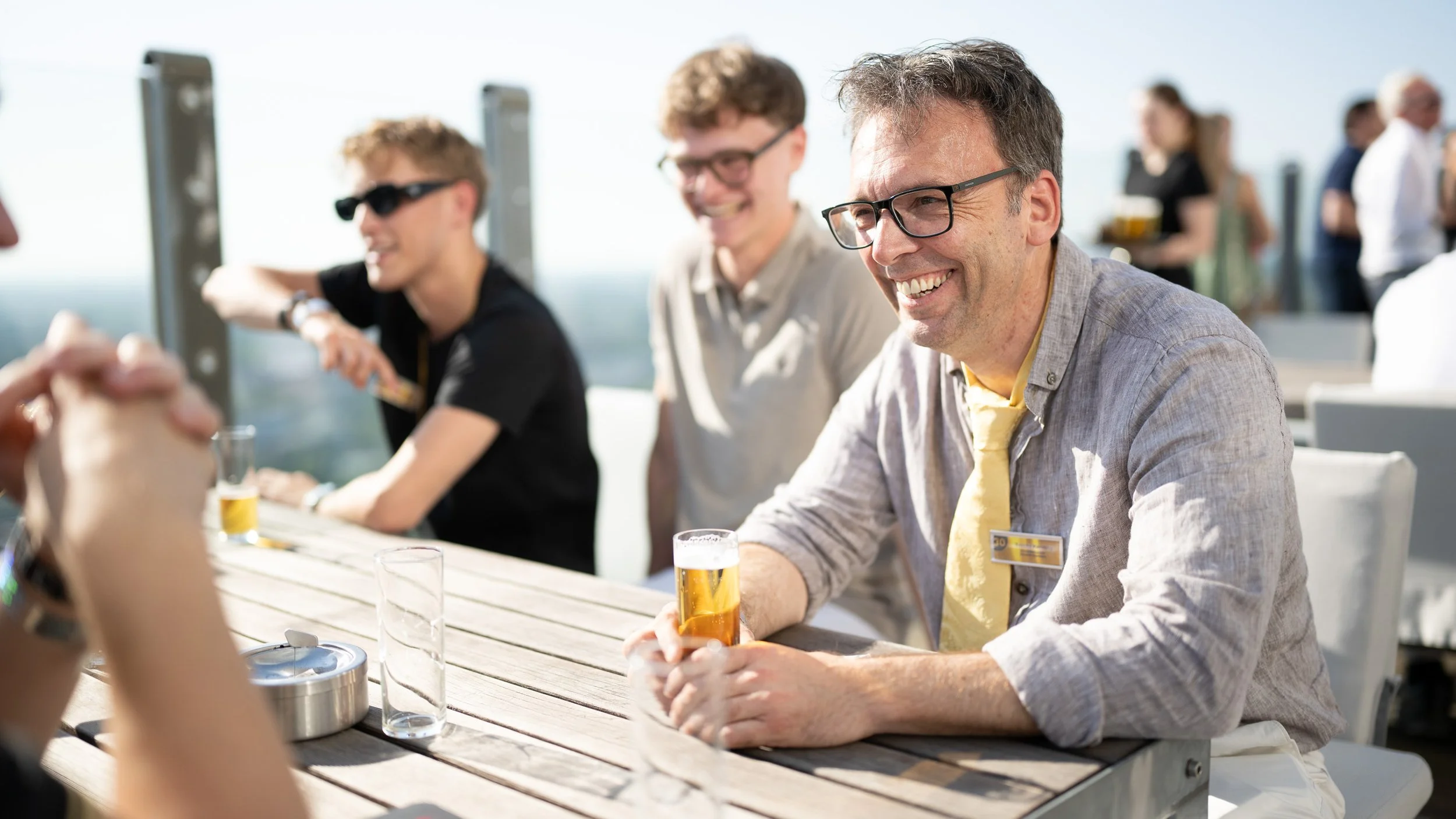 Gäste stoßen mit Bier auf einer sonnigen Dachterrasse bei einer Firmenfeier am media park in koeln an