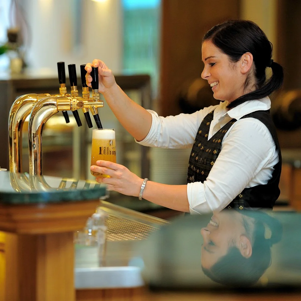 Mitarbeiterin zapft ein Bier an der Hotelbar – Unternehmensportrait im Gastgewerbe in Köln und Bonn.