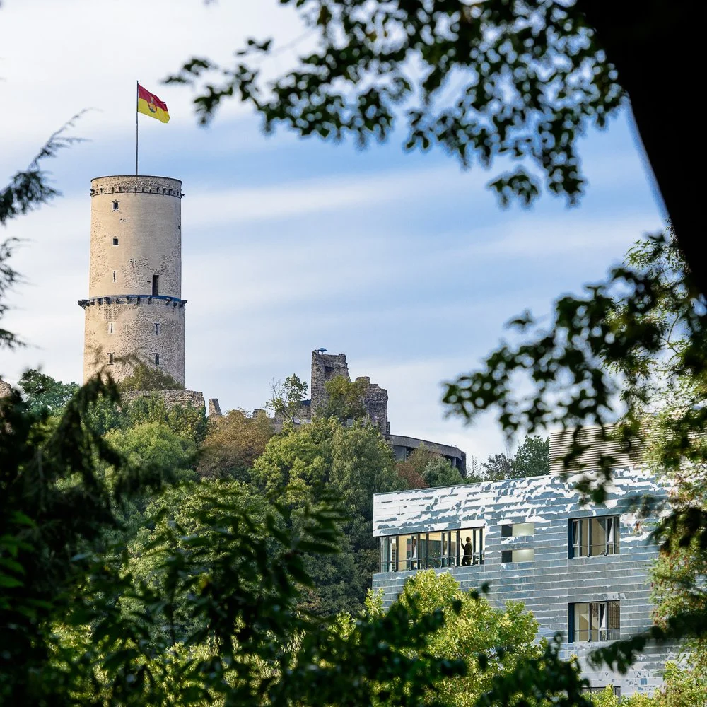 Historischer Turm zwischen Bäumen vor blauem Himmel – Architekturfotografie eines Baudenkmals