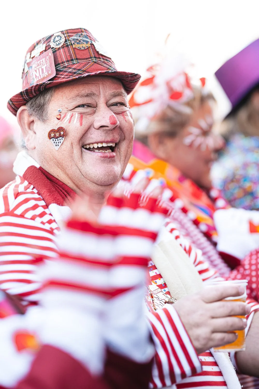 Lachender Jeck mit Schminke und rot-weißem Kostüm beim Karneval.