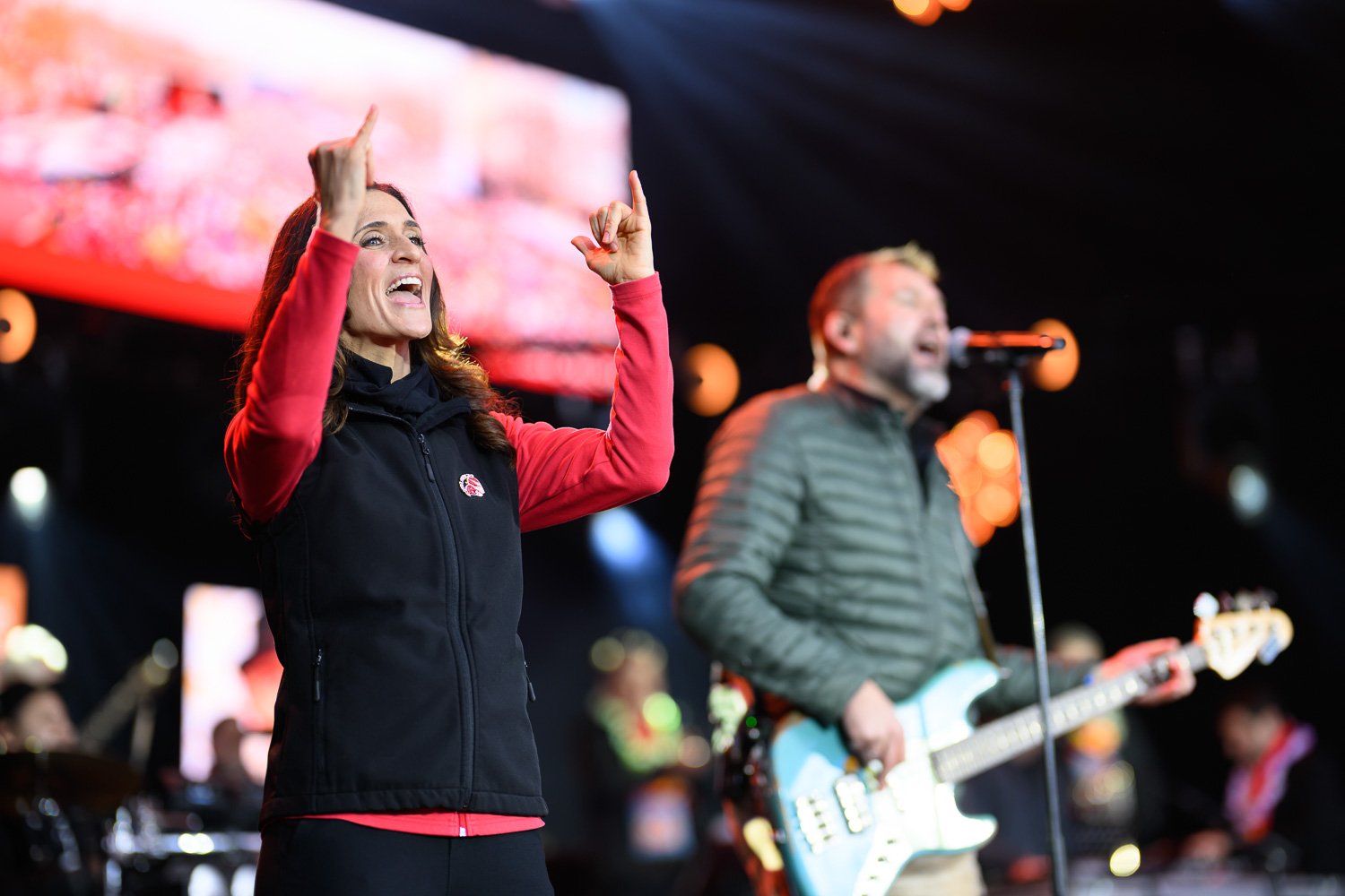 Gebärdendolmetscherin im Vordergrund übersetzt einen Open-Air-Auftritt auf der Bühne, Musiker im Hintergrund