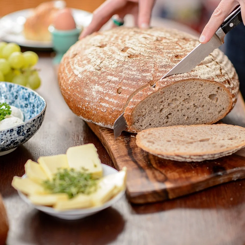 Frisch aufgeschnittenes Landbrot mit Kräuterbutter auf einem Holzbrett – Food-Fotografie im Set