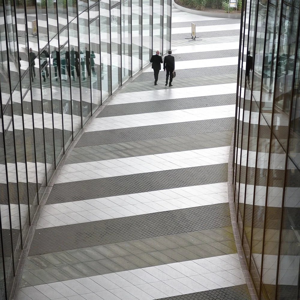 Langer Korridor mit diagonalem Licht-Schatten-Muster und Personen – Architekturfotografie mit klarer Linienführung