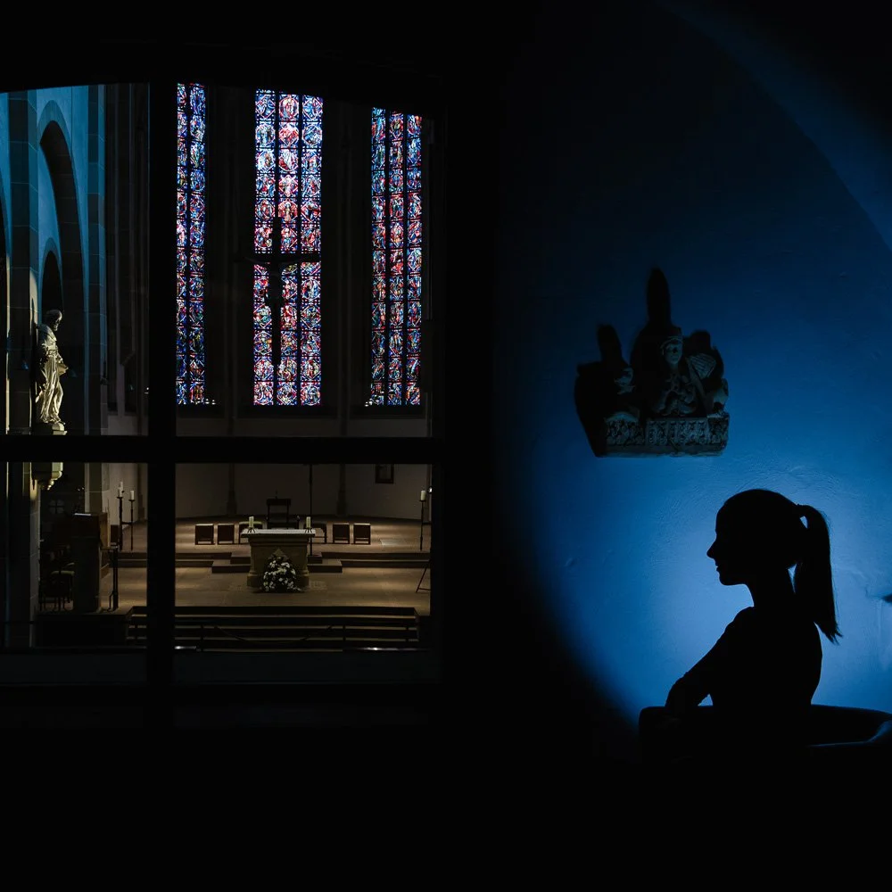 Dunkler Raum mit farbig leuchtenden Fenstern und Silhouette – Architekturfotografie mit atmosphärischer Lichtstimmung