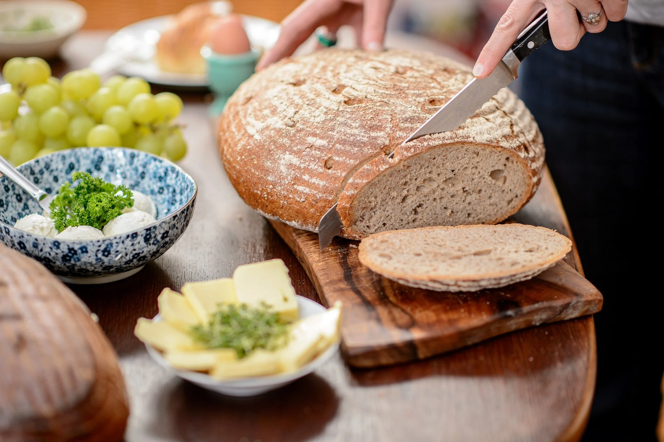 Frisch aufgeschnittenes Landbrot mit Kräuterbutter auf einem Holzbrett – Food-Fotografie im Set