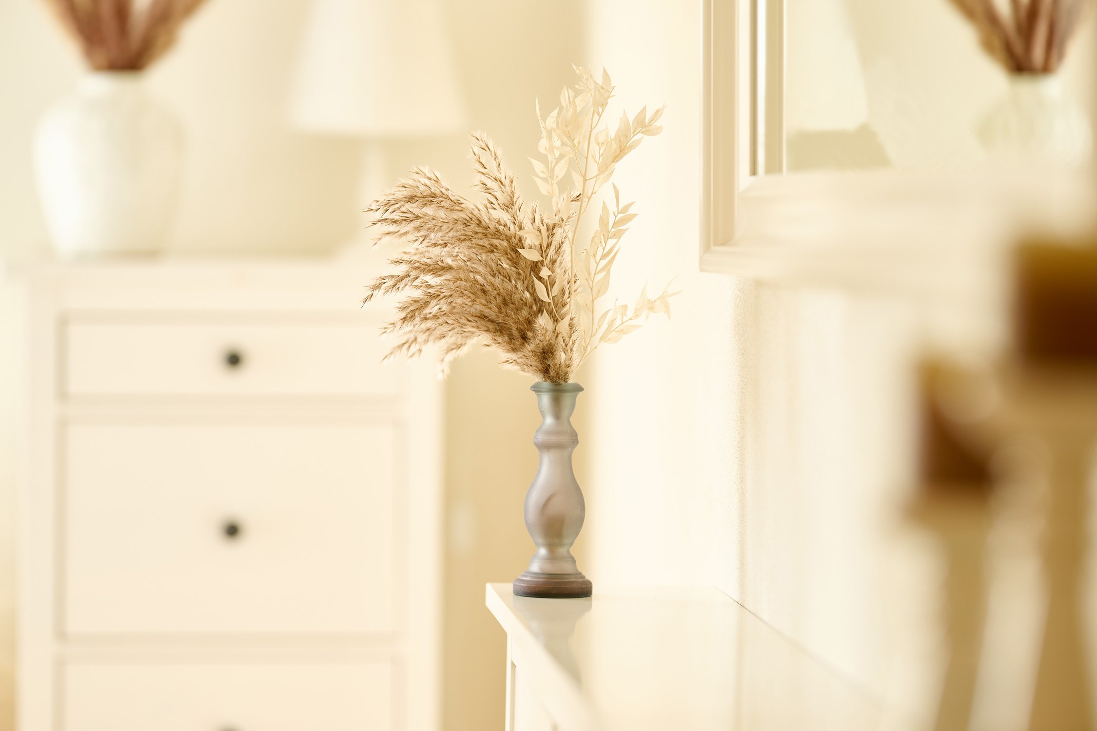 Trockengräser in einer Vase auf einer hellen Kommode – Interior-Fotografie im warmen Licht