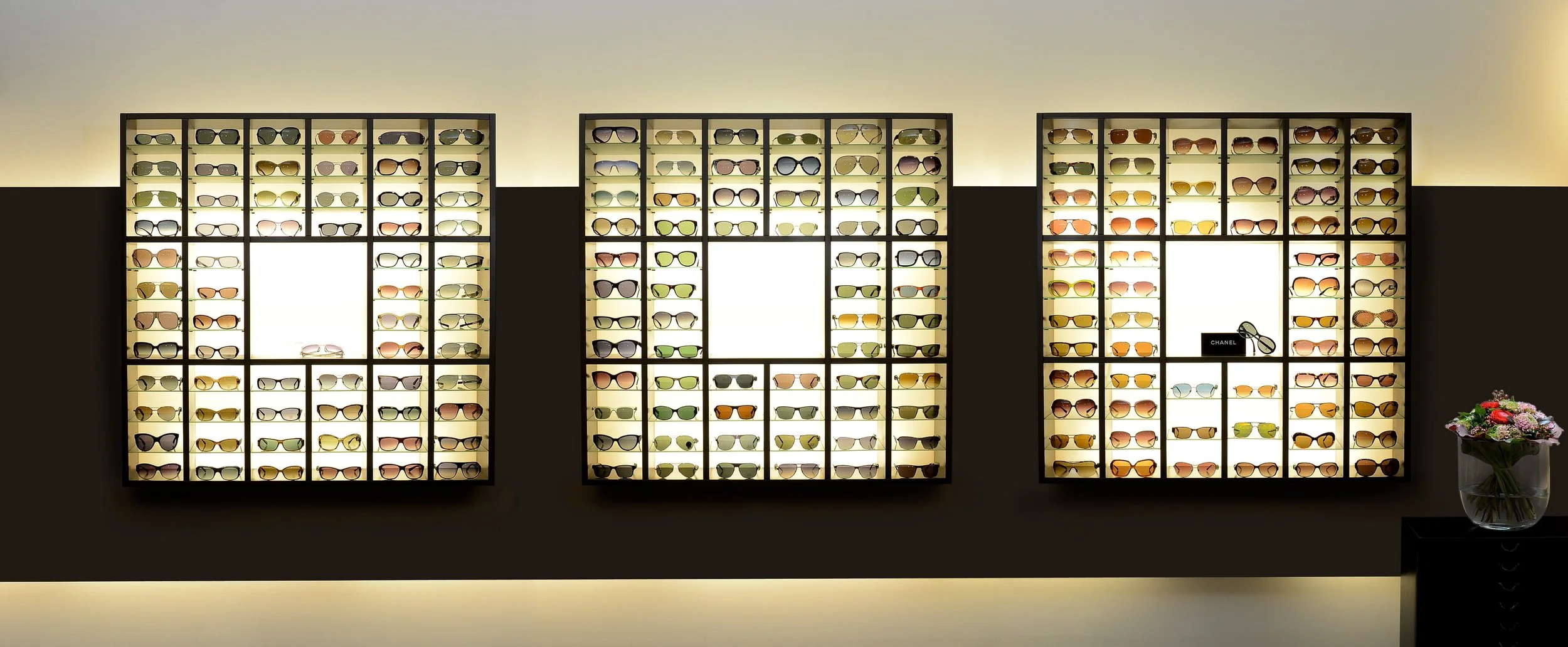 Drei beleuchtete Wand-Displays mit Sonnenbrillen in einem Optiker-Geschäft – Innenarchitektur- und Ladenbau-Fotografie in Bonn