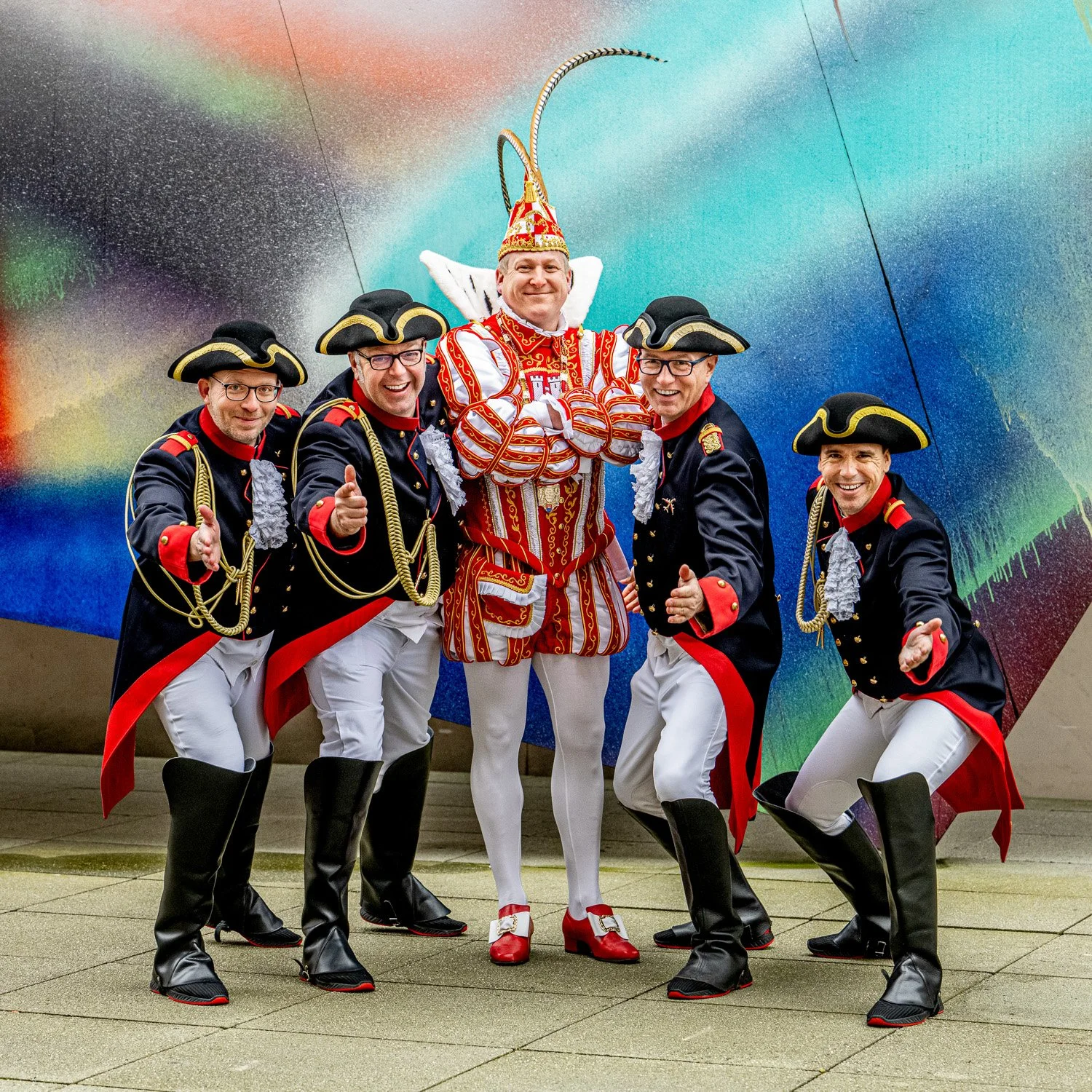 Karnevalsprinz mit Gefolge vor einer Graffiti-Wand.