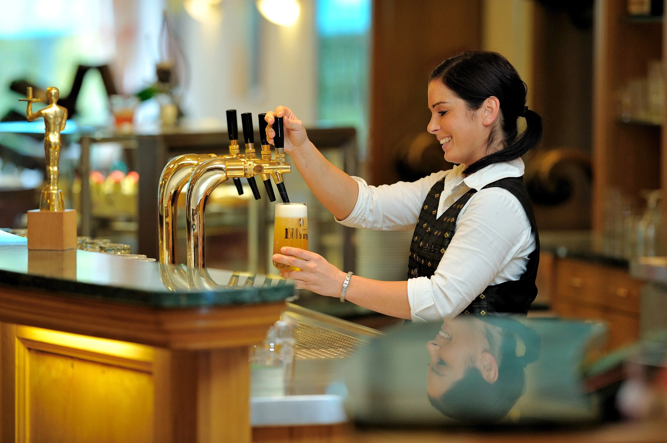 Mitarbeiterin zapft ein Bier an der Hotelbar – Unternehmensportrait im Gastgewerbe in Köln und Bonn.