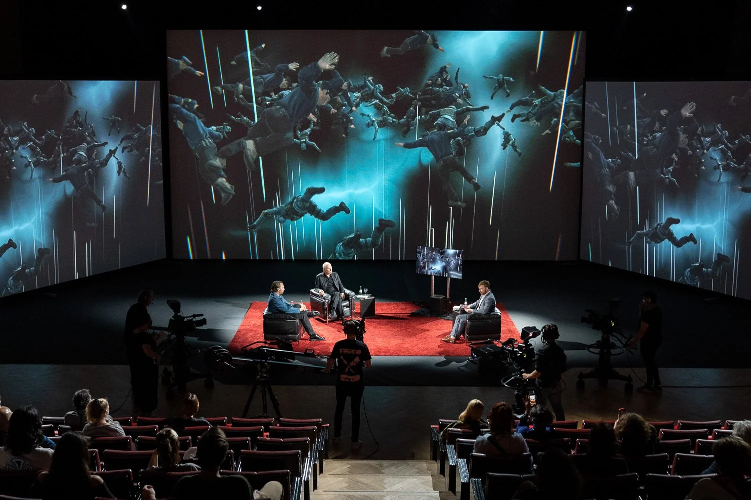 Weite Theaterbühne mit Projektionsleinwand während einer Abendveranstaltung.