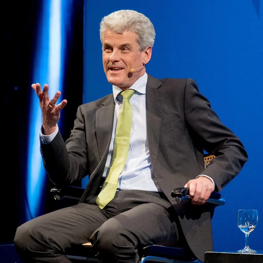 Redner im Anzug sitzt auf der Bühne und spricht bei einer Talkrunde.