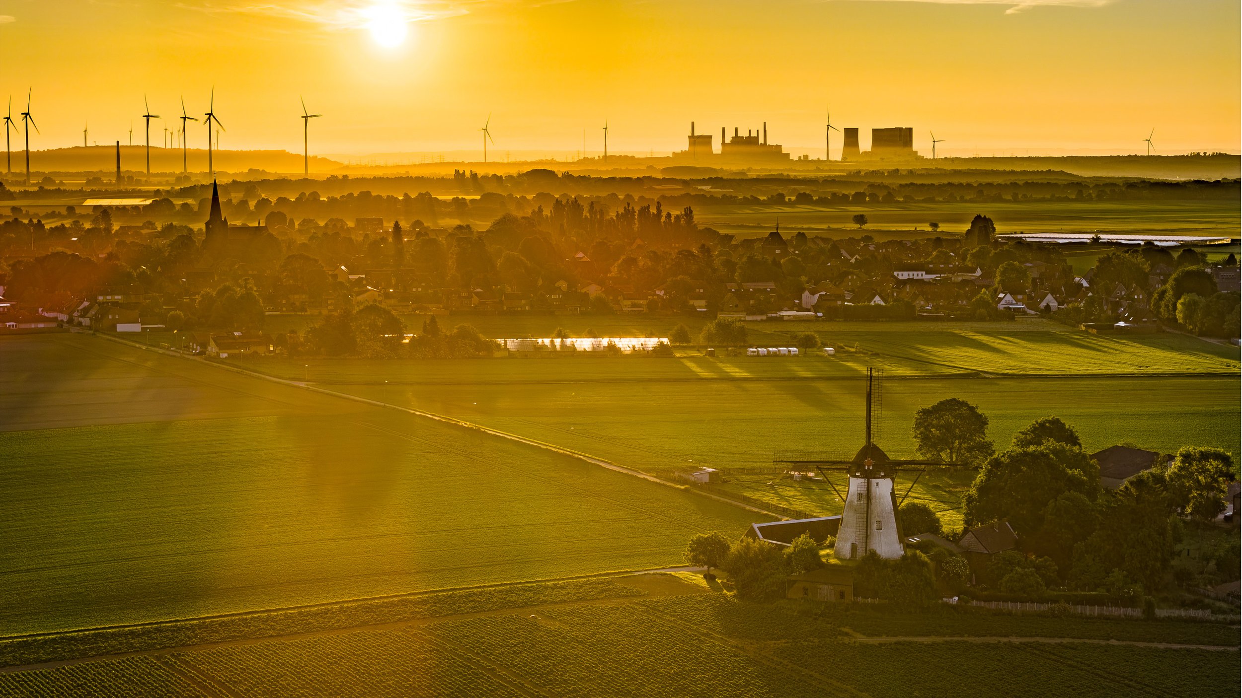 Luftaufnahme einer Windmühle in goldenem Abendlicht mit Windrädern am Horizont – Drohnenfotografie am Niederrhein
