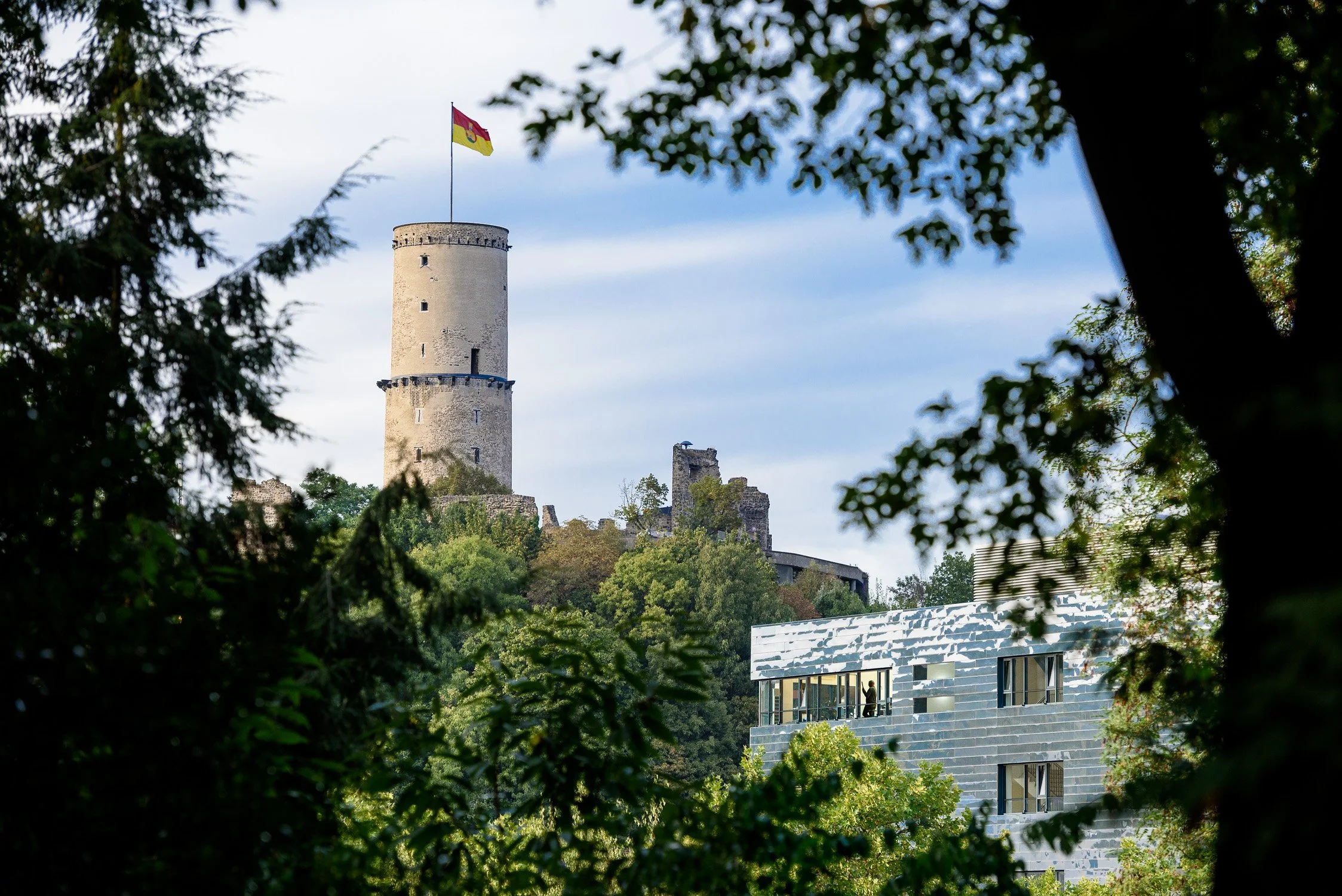 Historischer Turm zwischen Bäumen vor blauem Himmel – Architekturfotografie eines Baudenkmals