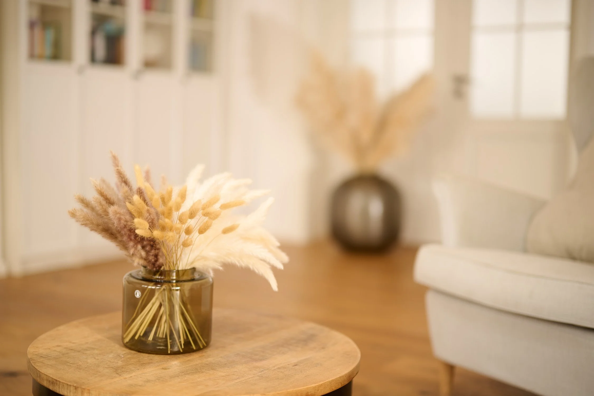 Trockengräser in einer Glasvase auf einem Beistelltisch im hellen Wohnraum – Interior- und Produktfotografie
