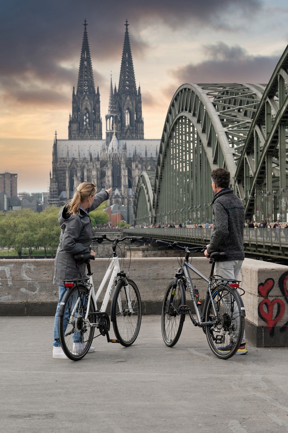 Radfahrer-Paar auf der Hohenzollernbrücke blickt zum Kölner Dom in der Abenddämmerung – Tourismusfotografie in Köln