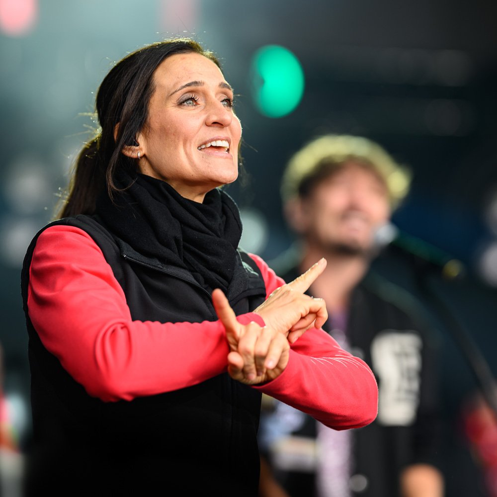 Gebärdendolmetscherin im Vordergrund übersetzt einen Bühnenauftritt, Musiker im Hintergrund