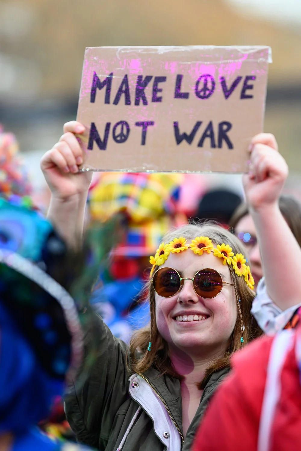 Jeck mit Sonnenbrille hält ein Schild mit der Aufschrift „Make Love Not War".
