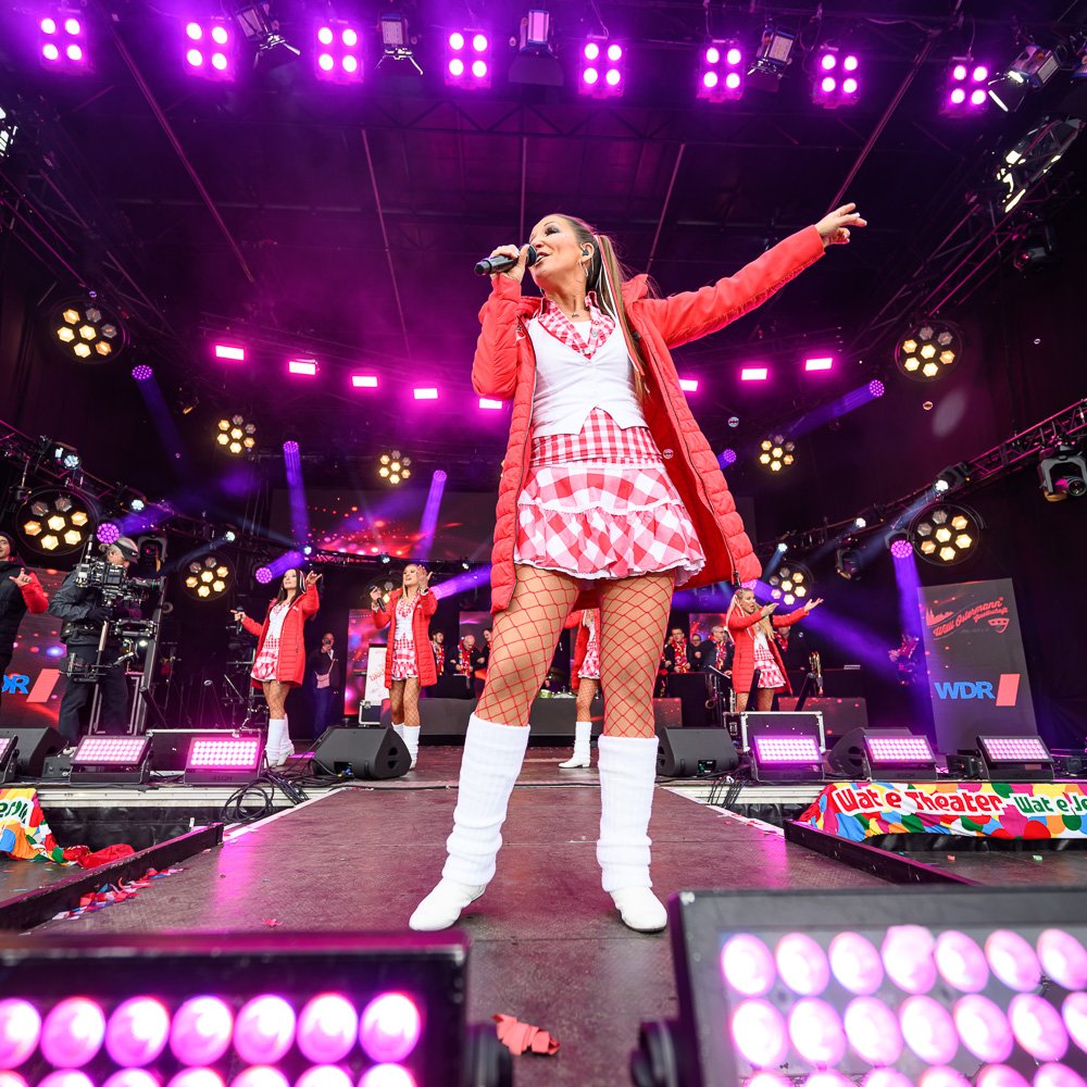 Live-Konzert: Sängerin im roten Outfit auf pink beleuchteter Bühne.