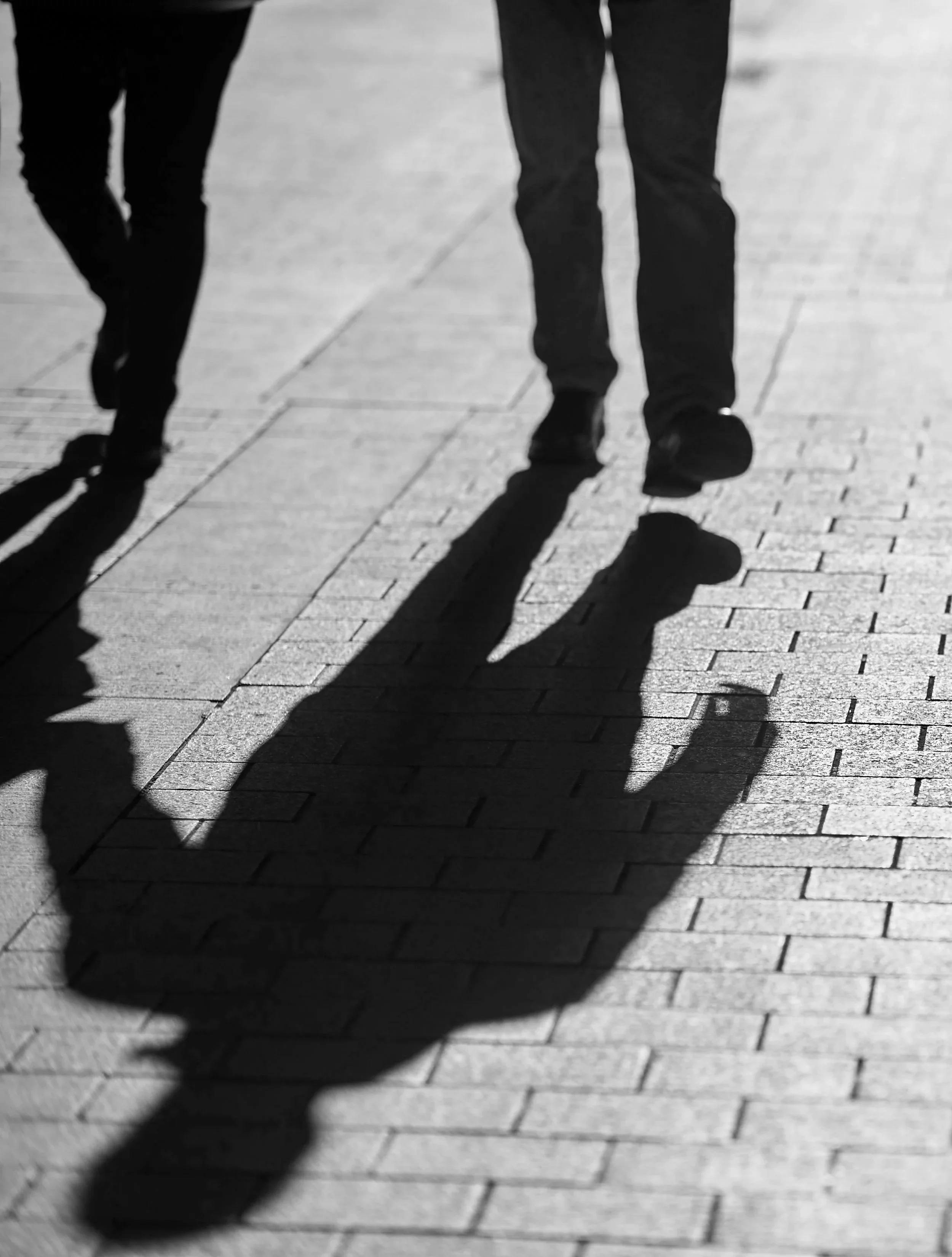 Silhouette of two people walking on a brick pavement, with their shadows cast on the ground.