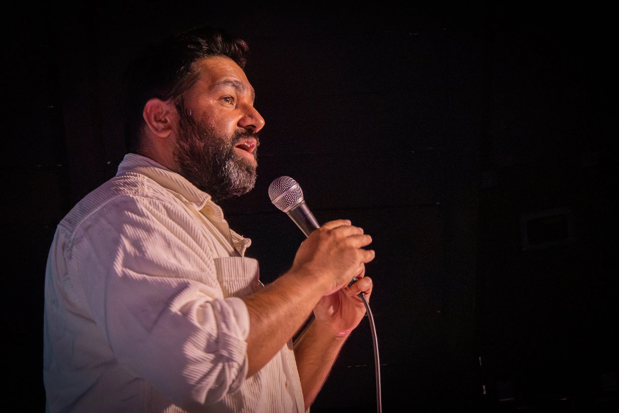 A man with a beard and earrings holding a microphone.