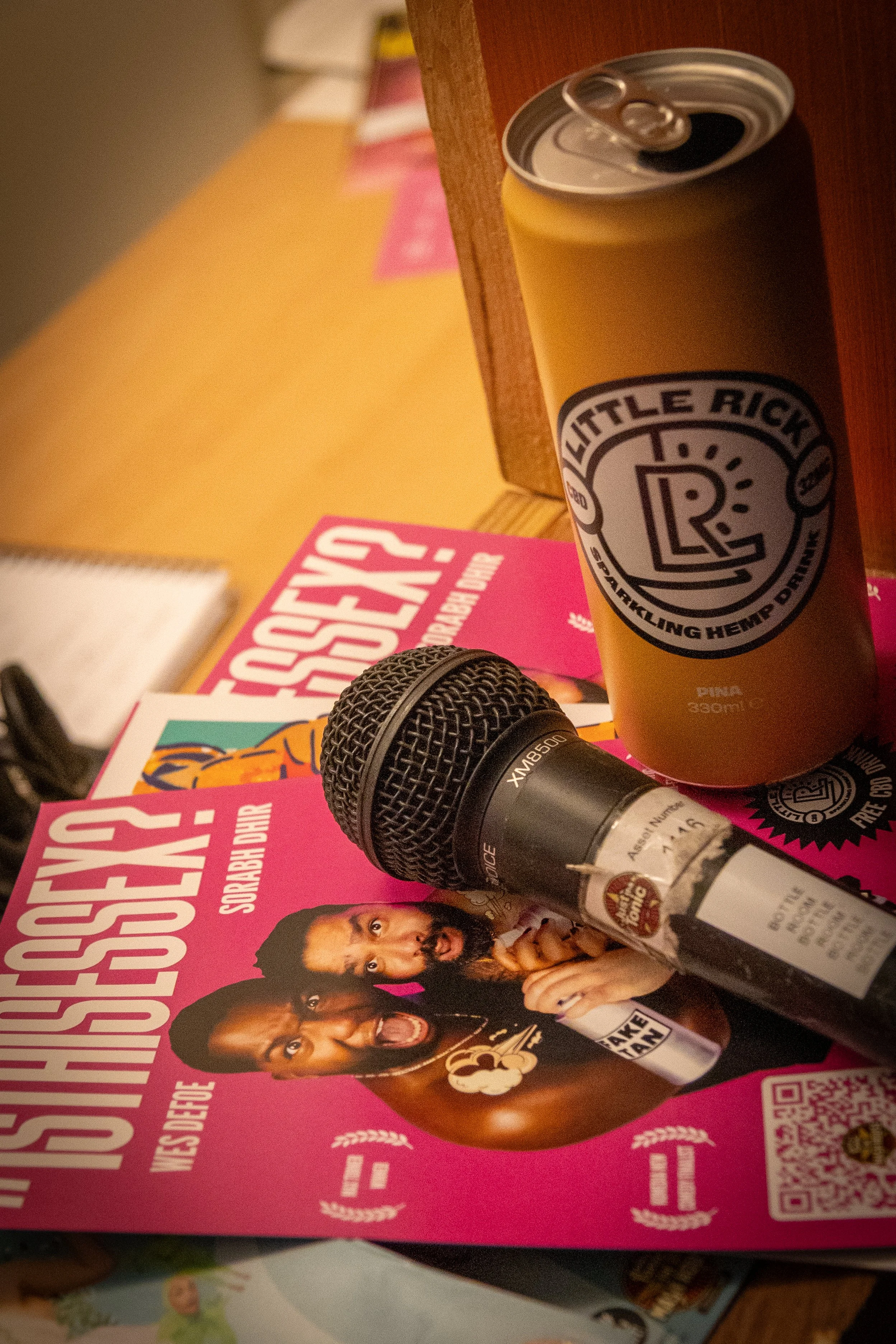 A can of Little Rick's sparkling hemp drink on a table next to a microphone and a magazine with a pink cover.