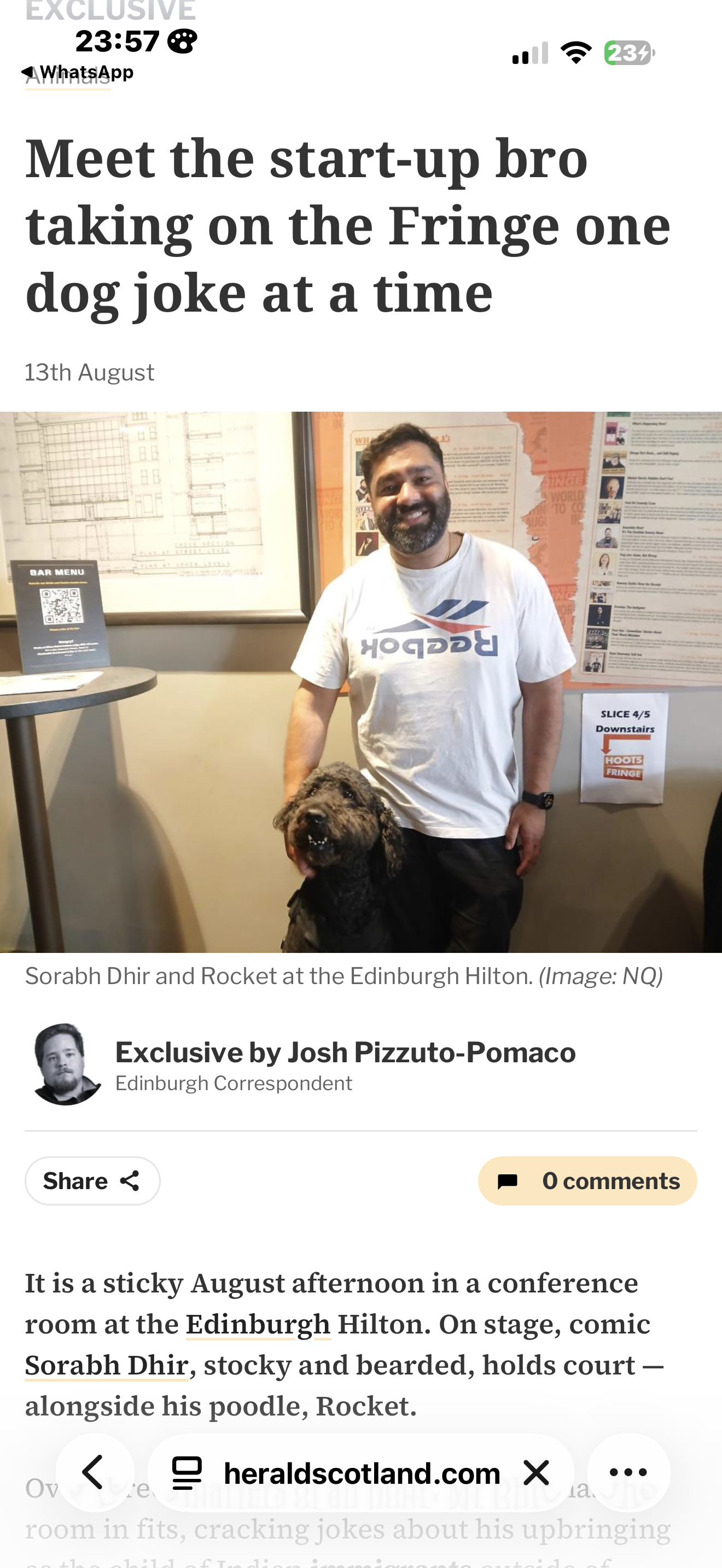 A man and a curly-haired dog standing together in a conference room at the Edinburgh Hilton. The man wears a white T-shirt with a logo and the dog is a poodle. There are posters and signage on the wall behind them.