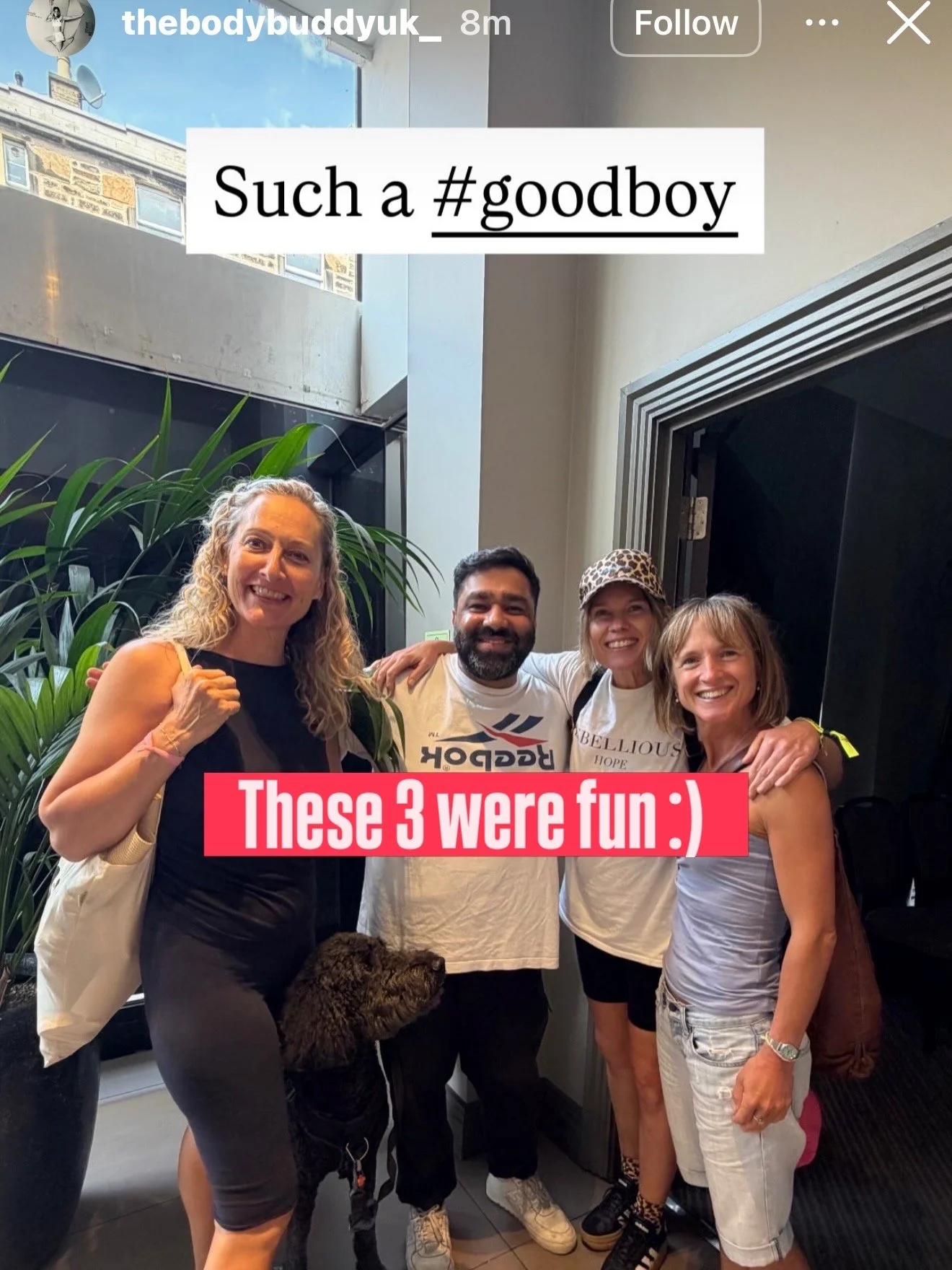 Four smiling people standing in a group indoors, with a large plant in the background. They are casually dressed, and one person is holding a dog. Text overlays read: 'Such a #goodboy' and 'These 3 were fun :).'