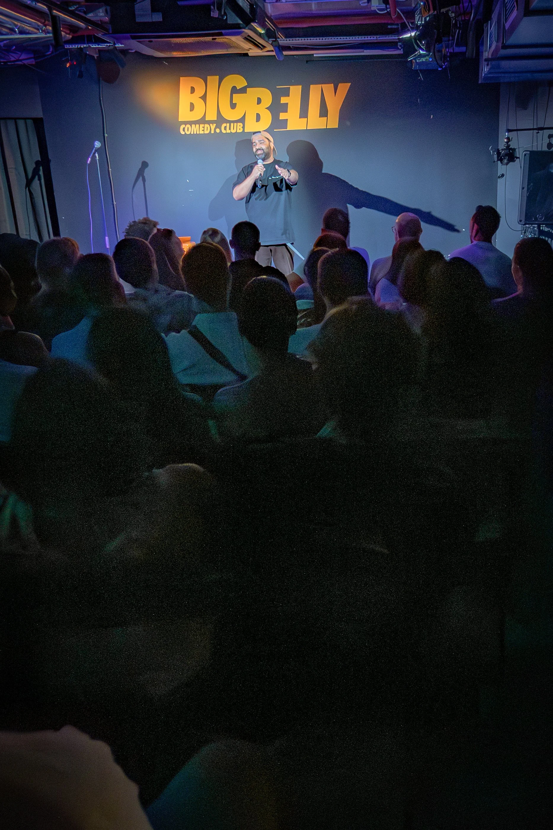 A comedian performs on stage at Big Belly Comedy Club with audience members watching.