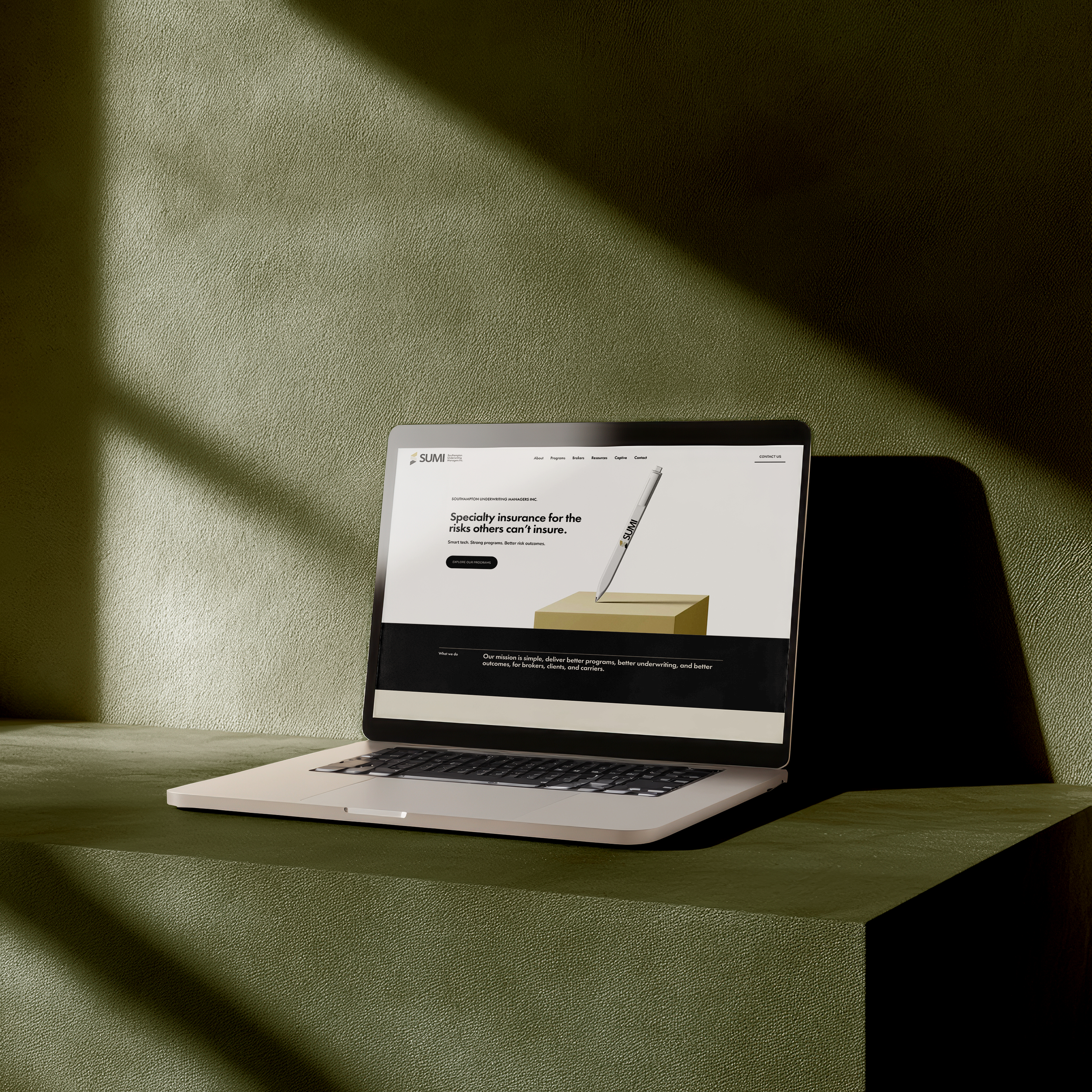 Partial view of a laptop computer on a green textured surface, displaying a webpage with text and imagery related to insurance services.